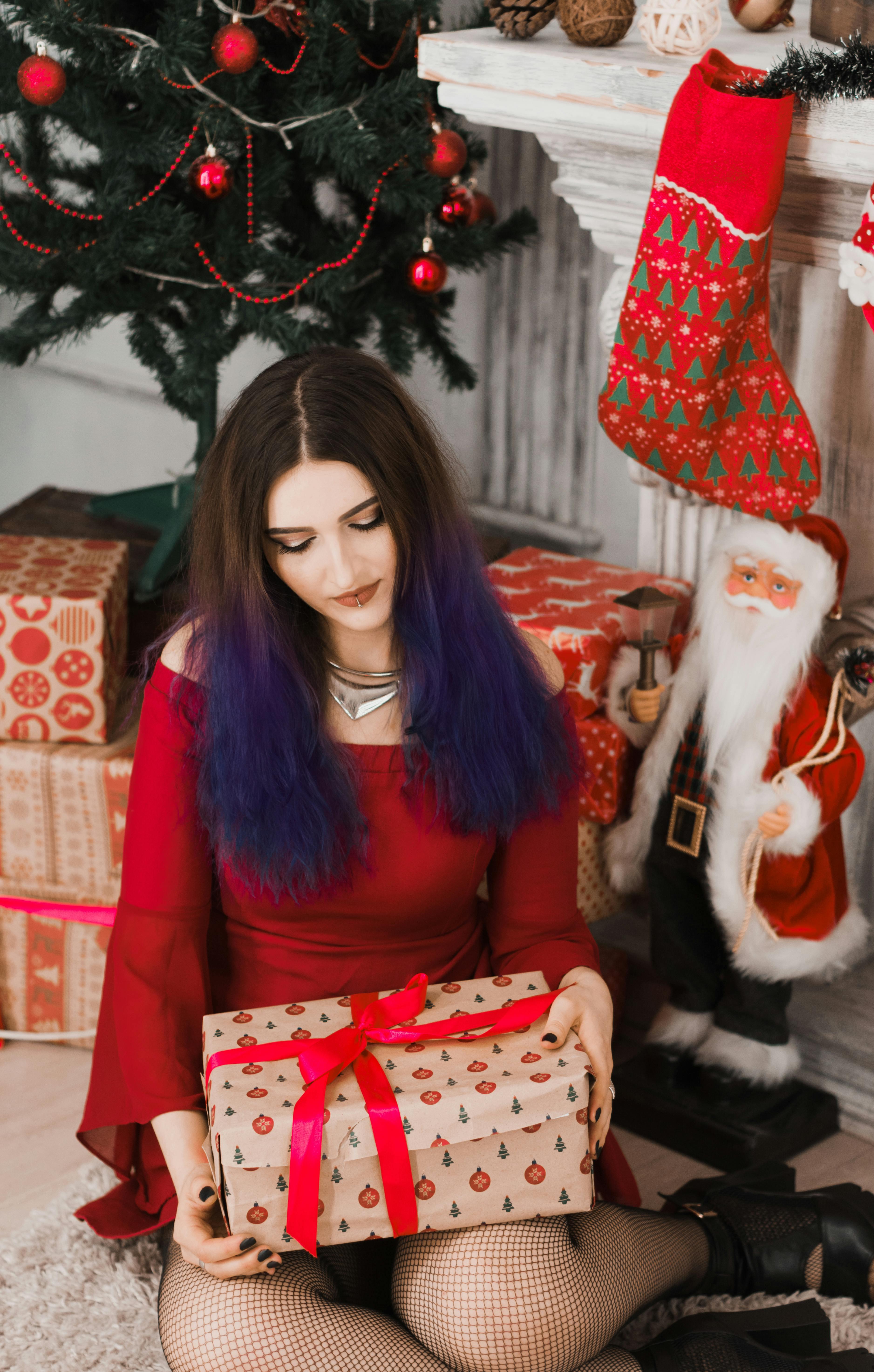Woman in festive attire holding a Christmas gift, surrounded by seasonal decorations.