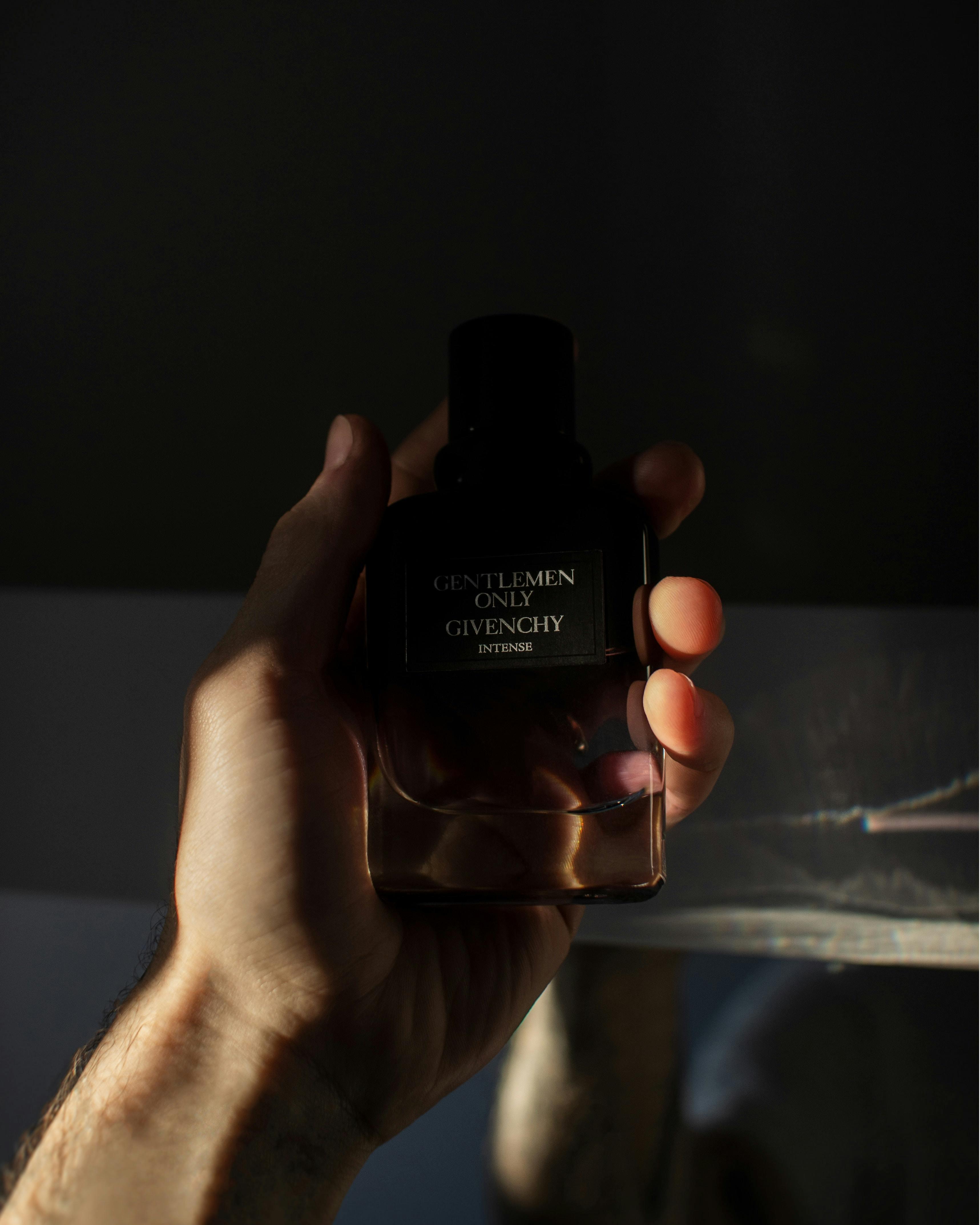 A man's hand holds a Givenchy perfume bottle with dramatic lighting.