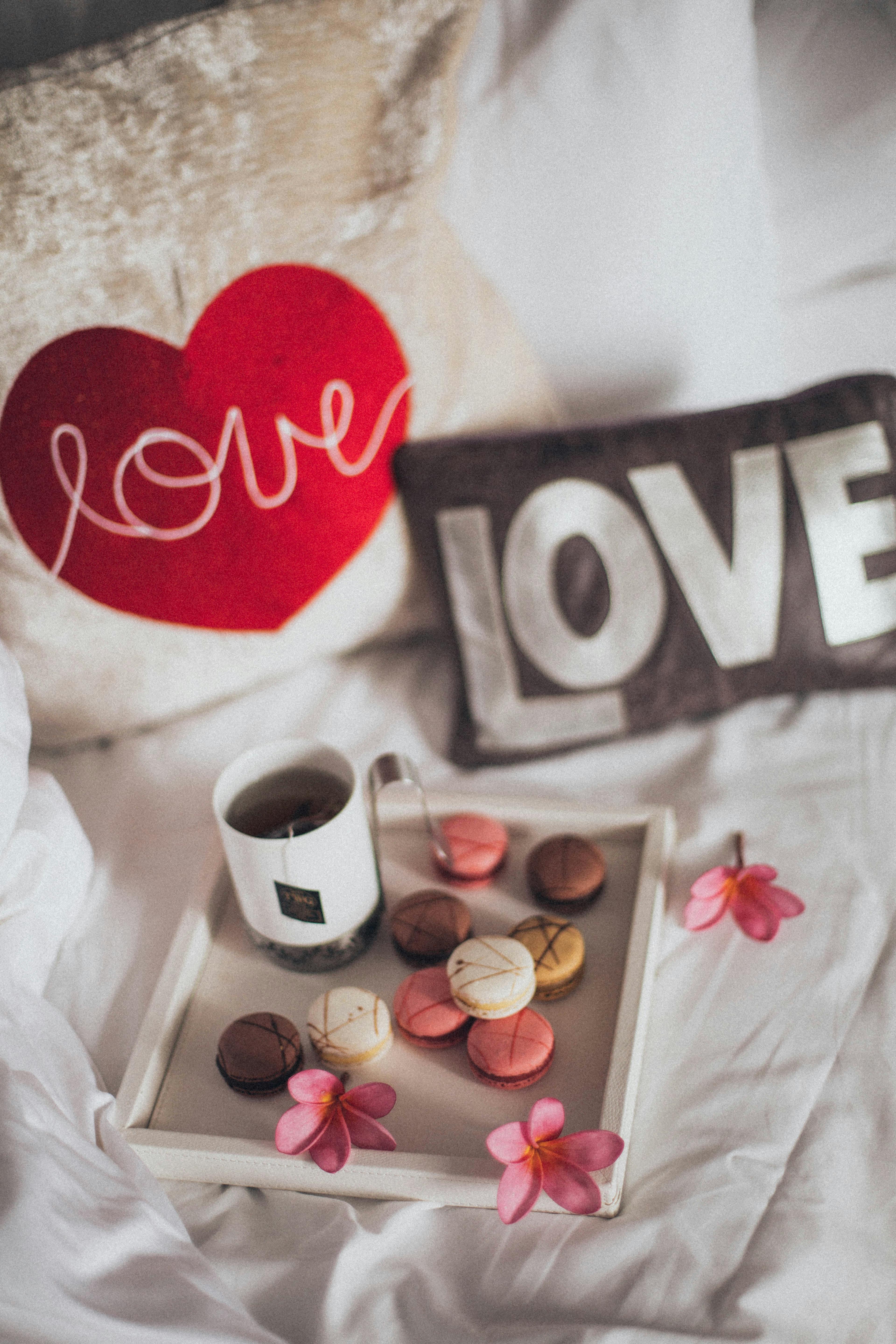 A cozy setup with coffee, macaroons, and decorative pillows on a bed. Perfect for relaxation.