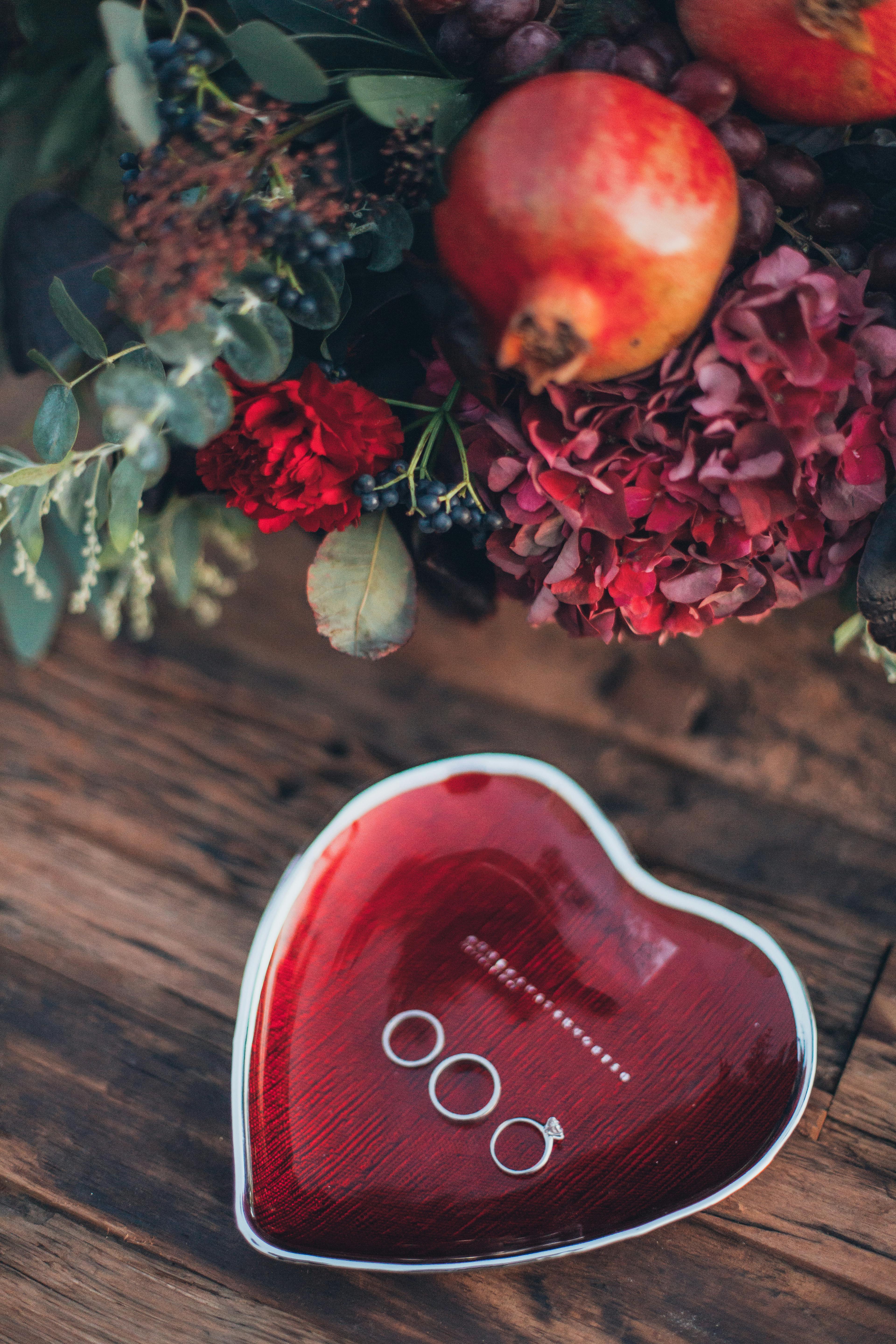 Heart-shaped jewelry box and pomegranate arrangement on wooden table, showcasing romantic decor.