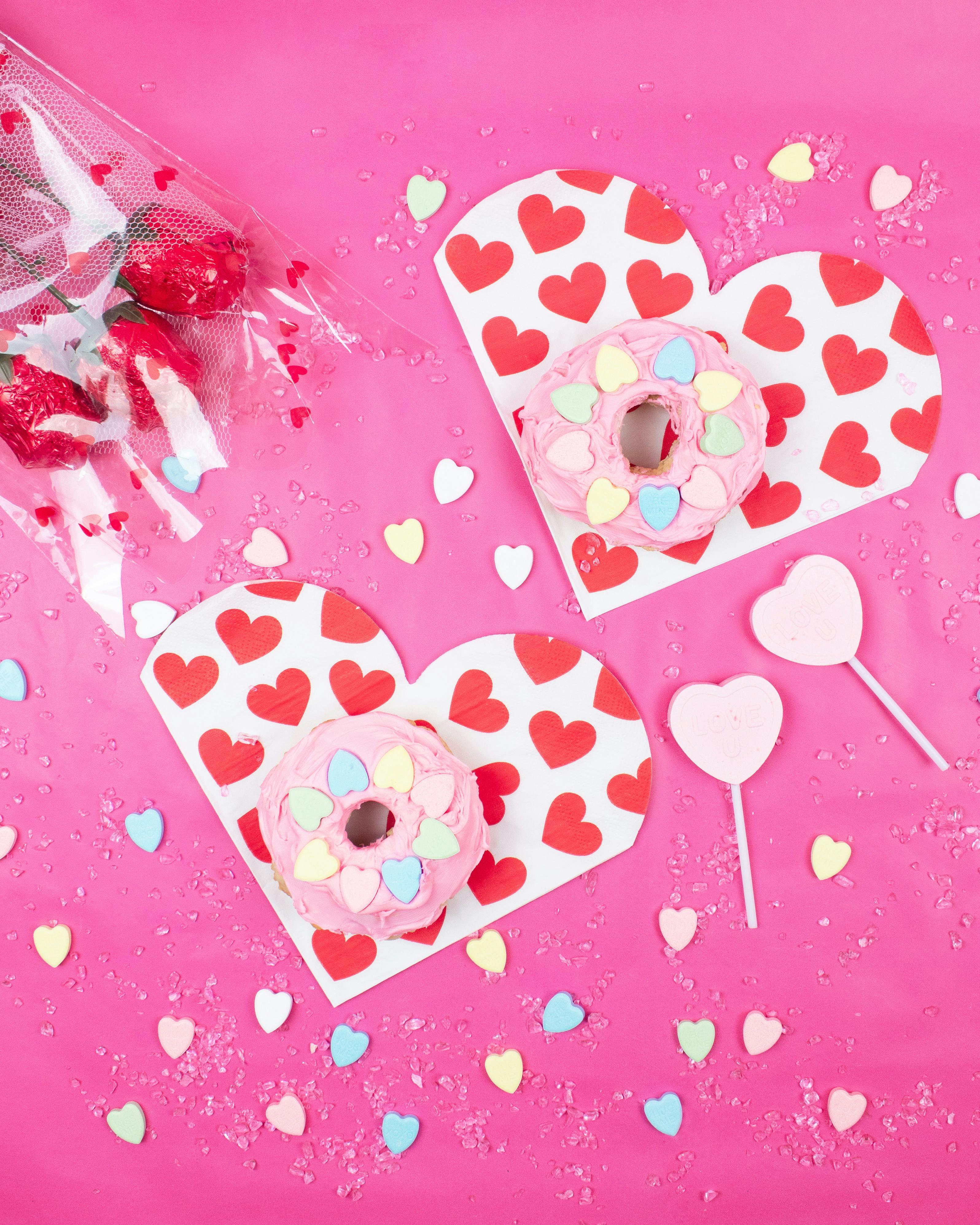 Bright and festive Valentine's Day setup with donuts and heart decor on pink background.