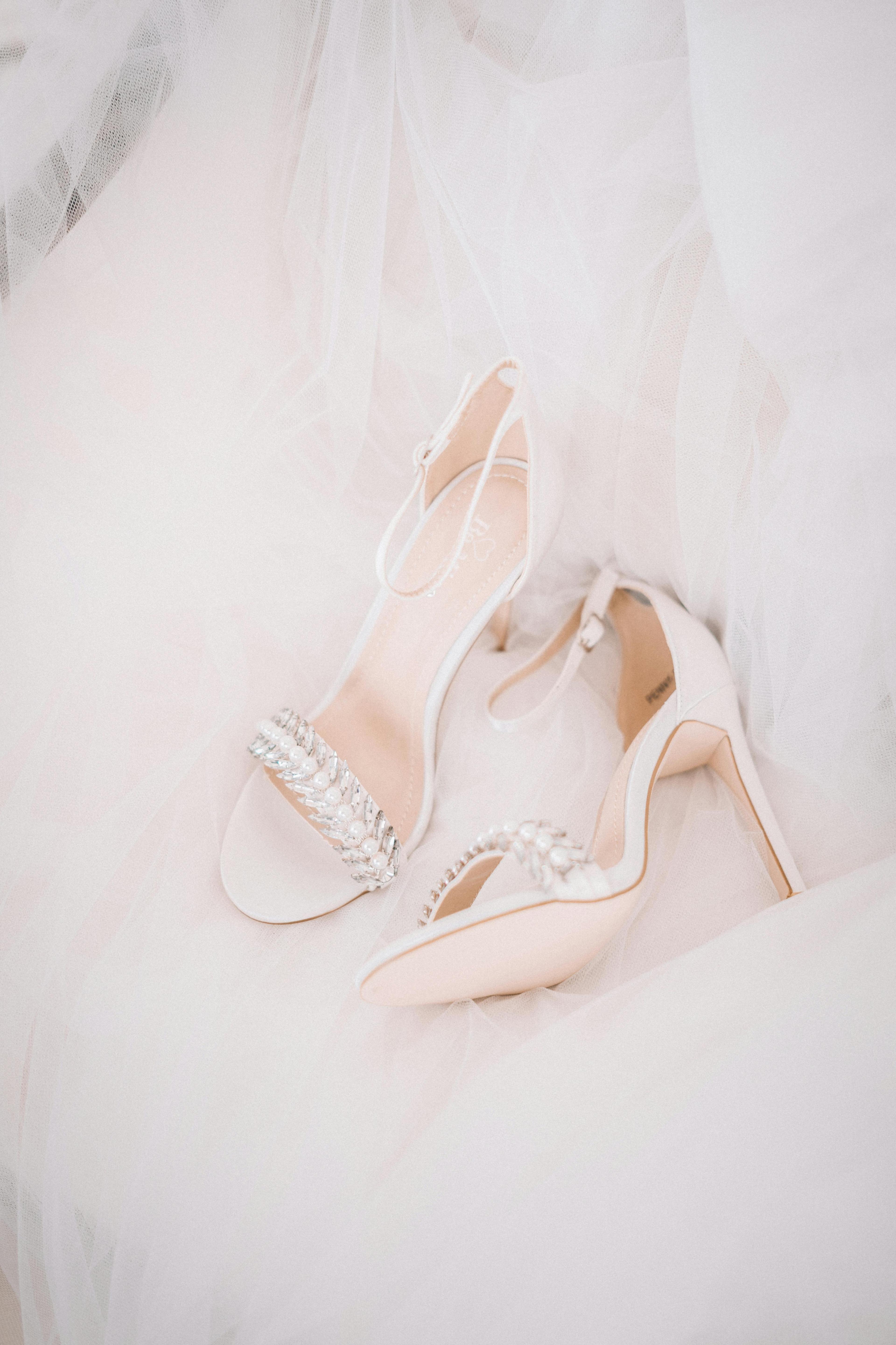 Close-up of elegant white wedding heels adorned with pearls on a flowing gown.