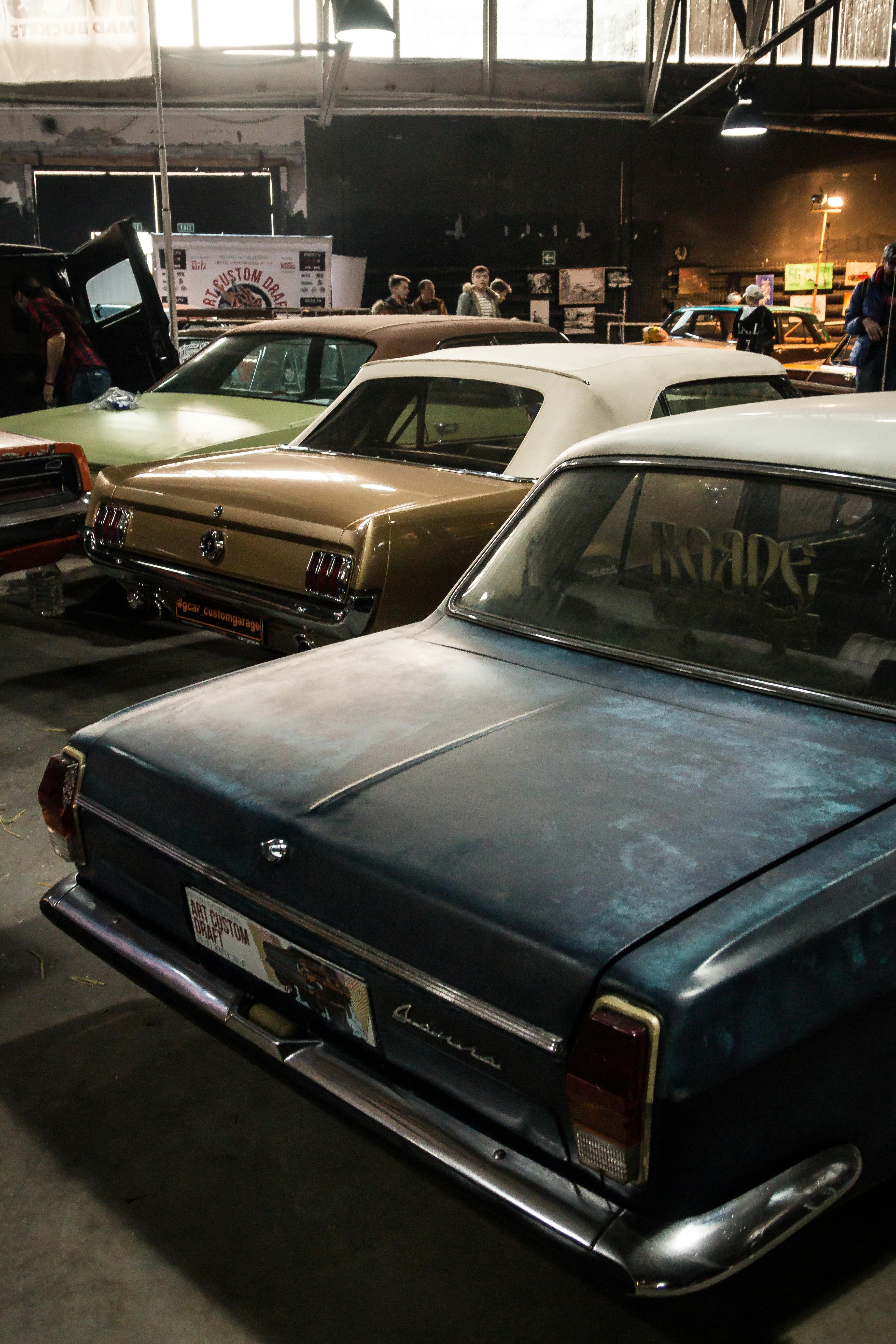 Explore a classic car show indoors featuring vintage sedans and automotive enthusiasts.