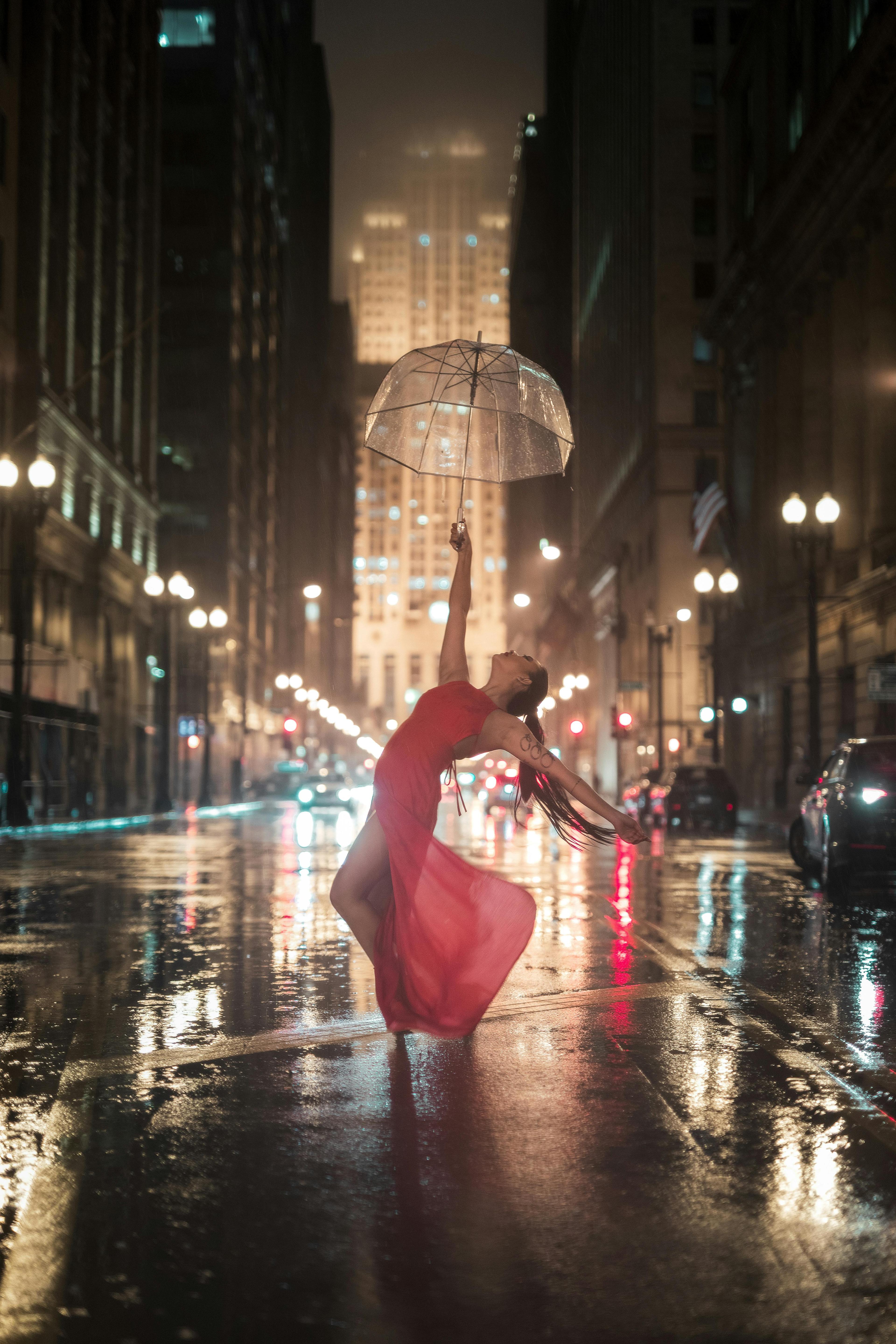 Nighttime urban scene with a dancer in a red dress posing gracefully on a wet street.