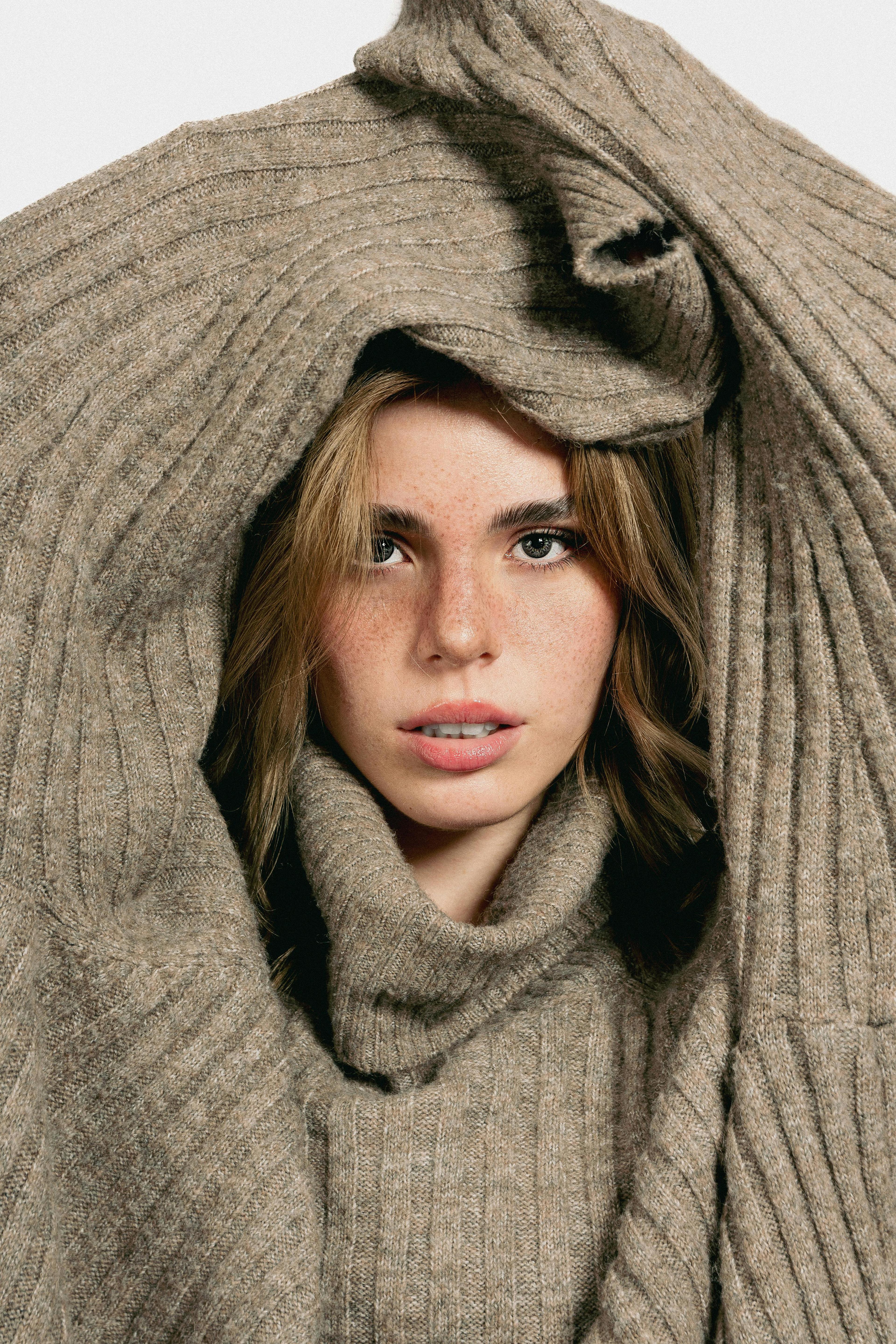 Close-up portrait of a woman framed by a cozy beige sweater for a warm, autumn fashion look.