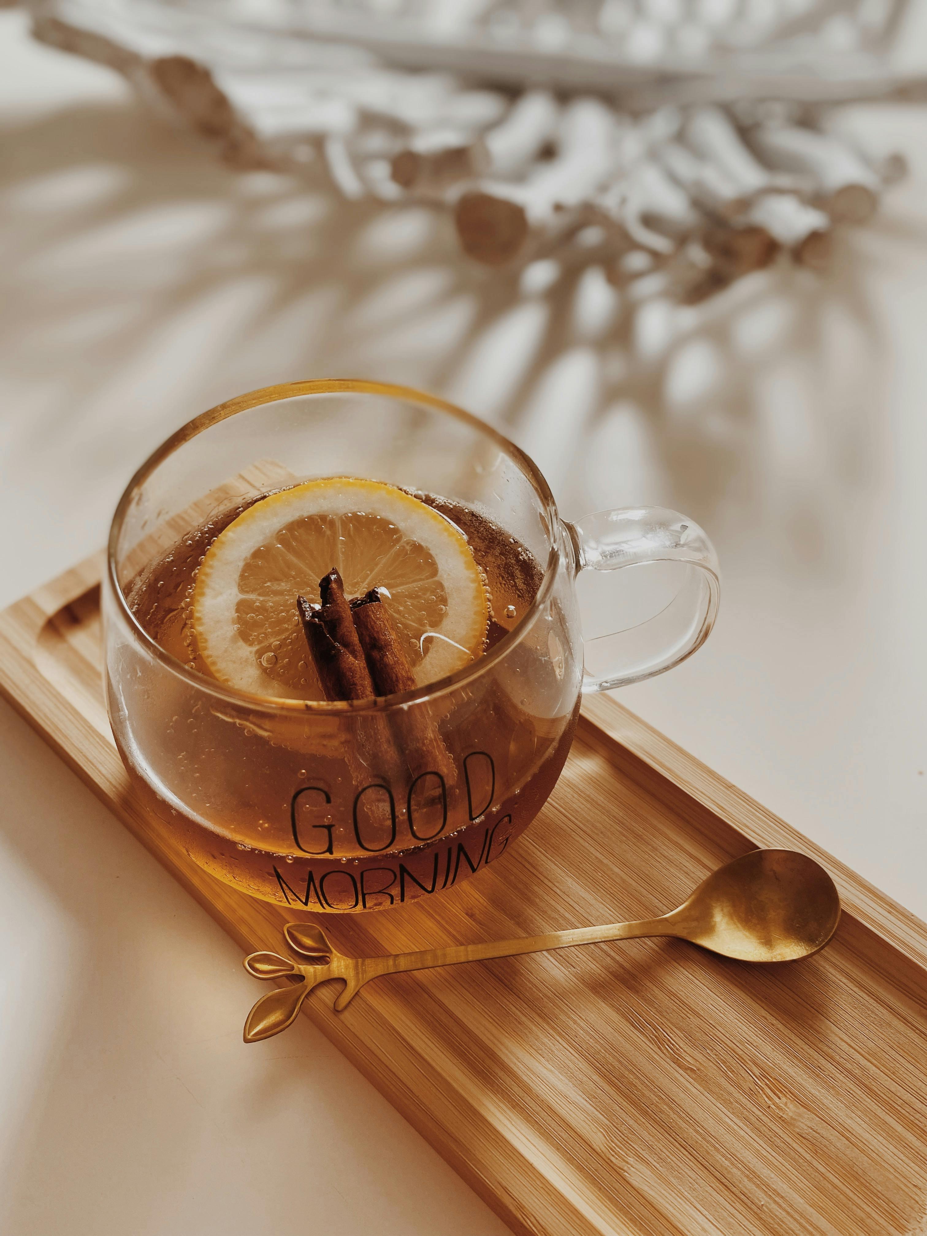 Warm cup of tea with lemon and cinnamon on a wooden tray for a cozy morning vibe.