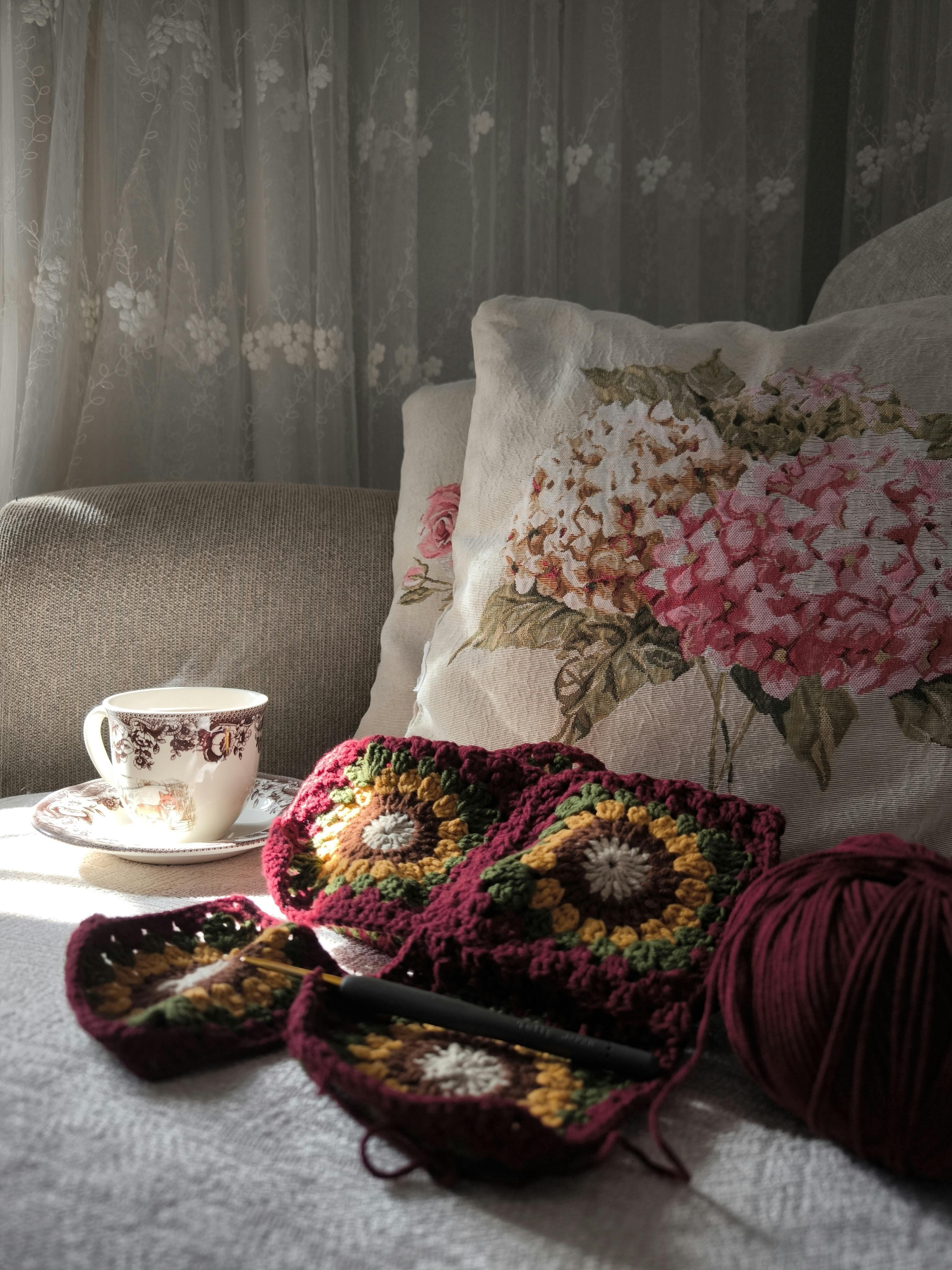 Inviting crochet and tea setup by an embellished floral pillow, perfect for relaxation.