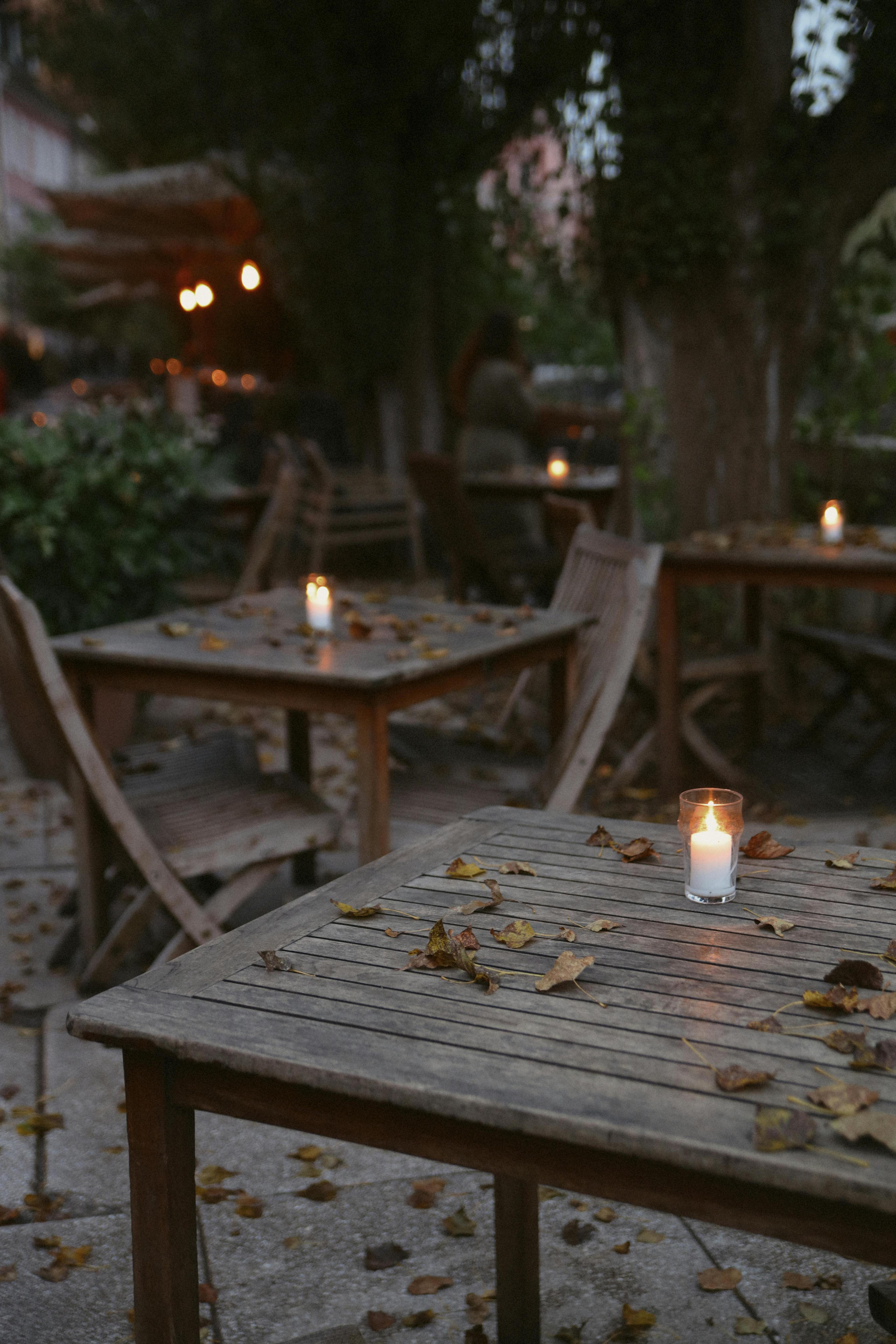 Rustic outdoor café setting with warm candlelight and fallen leaves on tables, creating a cozy atmosphere.