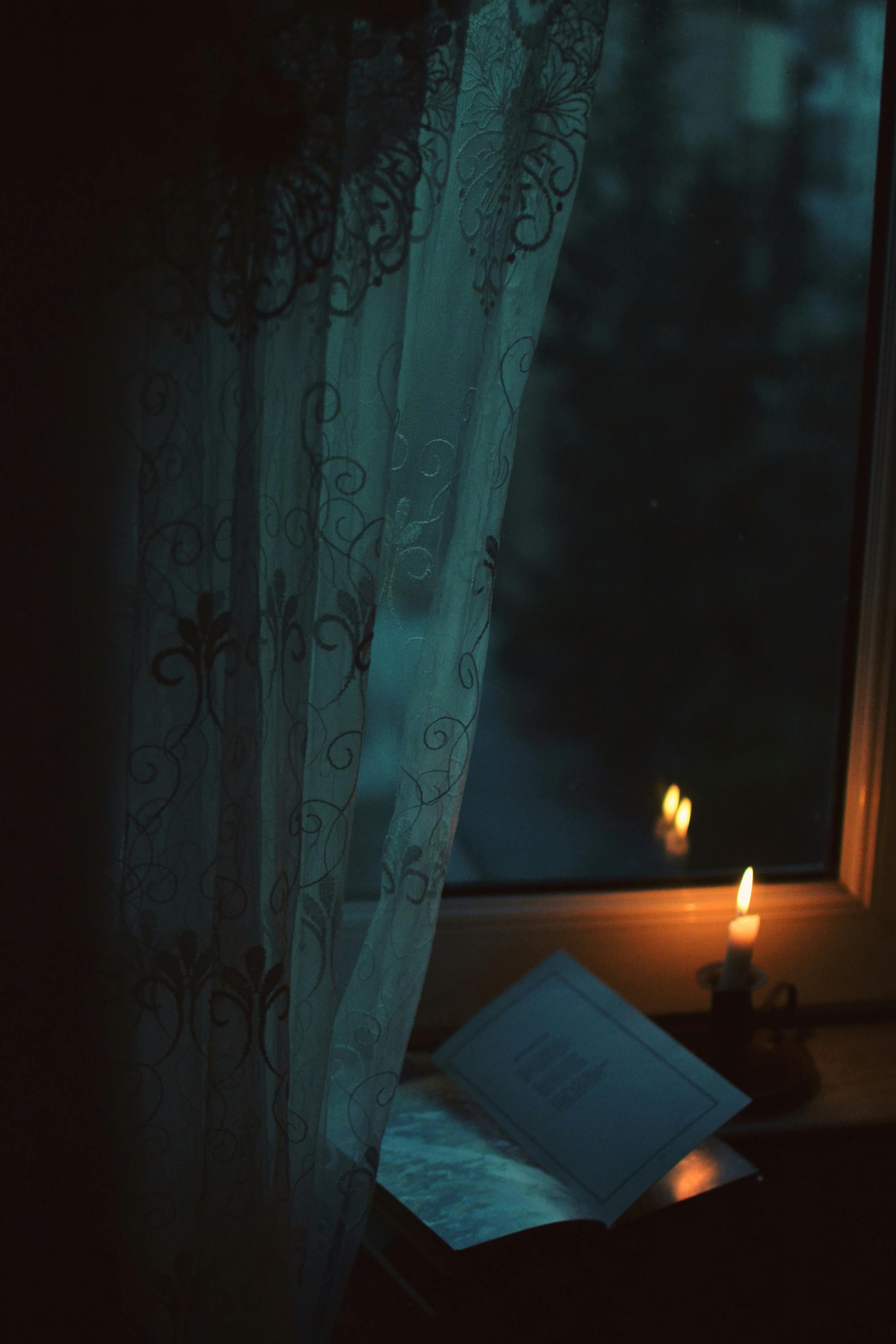 A peaceful scene with candlelight illuminating a book by a window at night.
