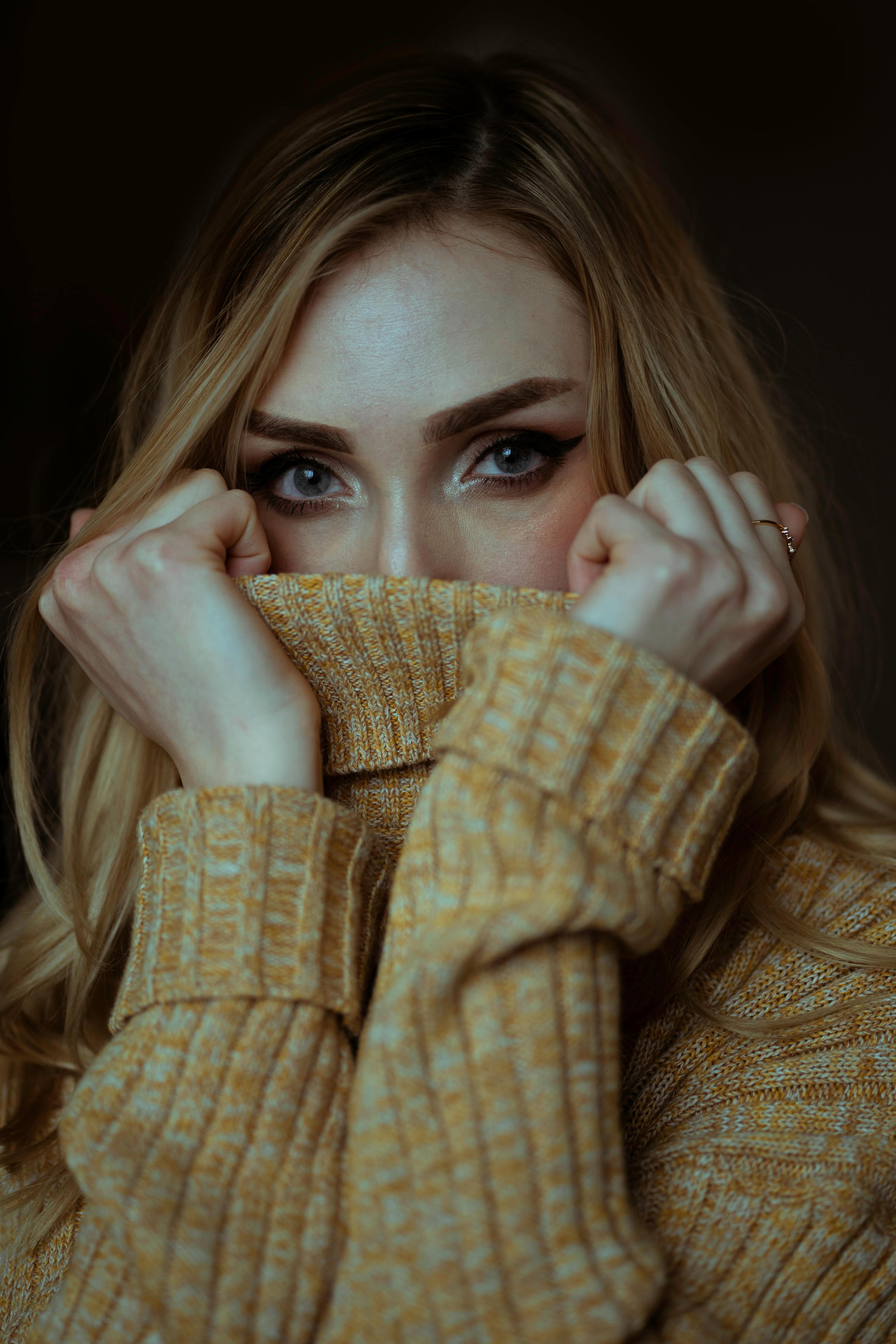 Intimate close-up shot of a woman covering her face with a sweater, highlighting her eyes.