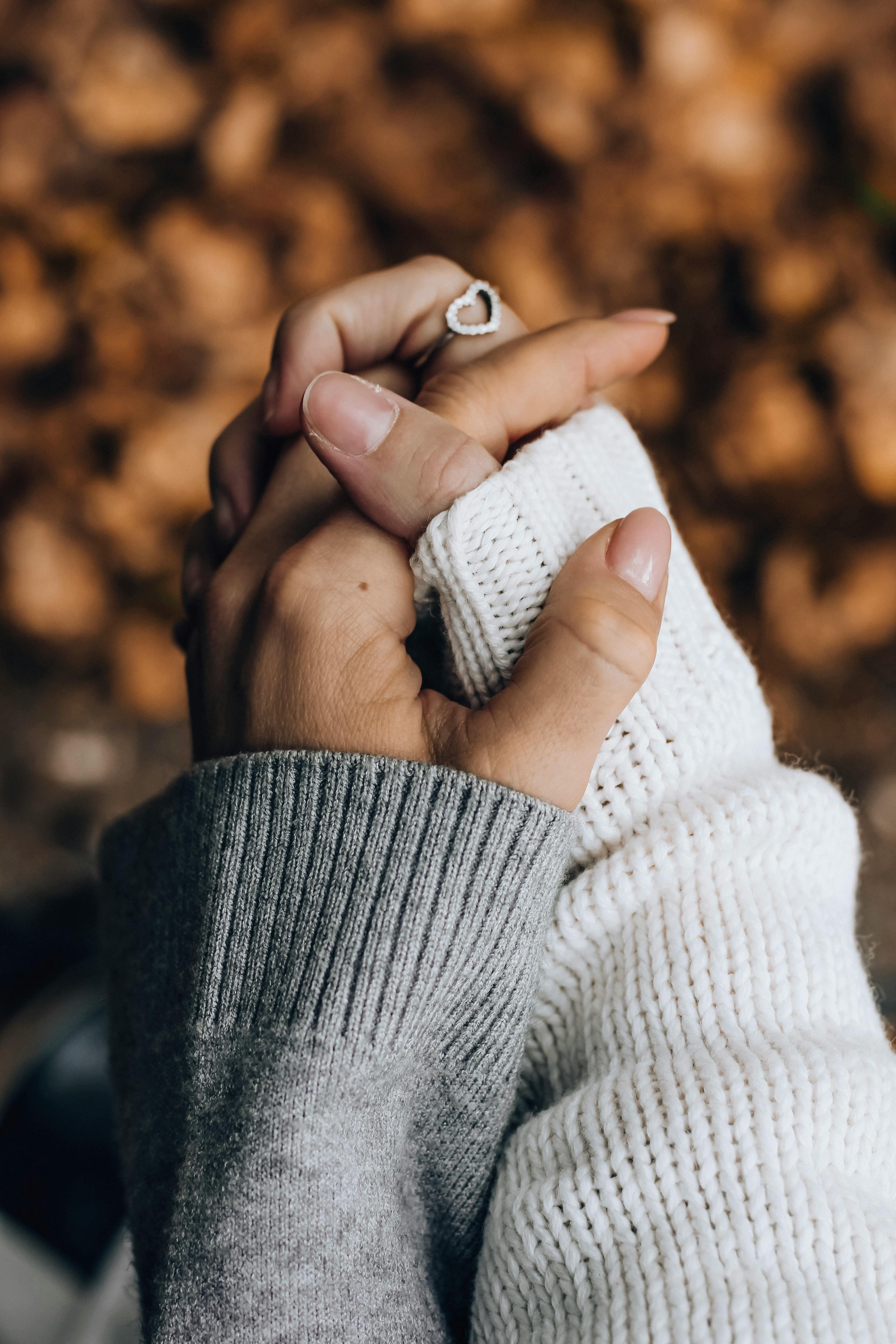 Close-up of two hands held together wearing cozy sweaters, a symbol of love and togetherness in fall.