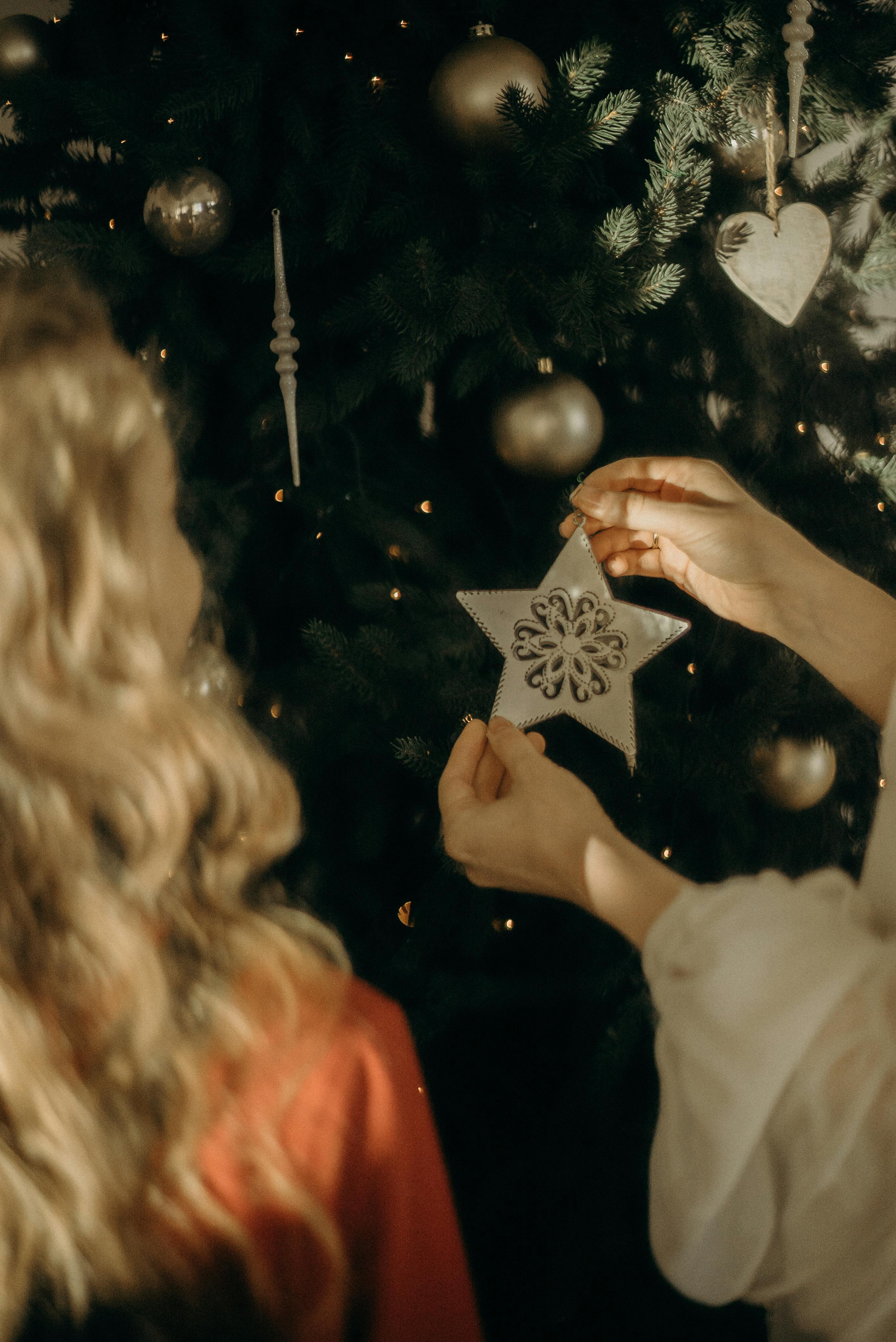 A woman places a star ornament on a Christmas tree, symbolizing festive holiday traditions.