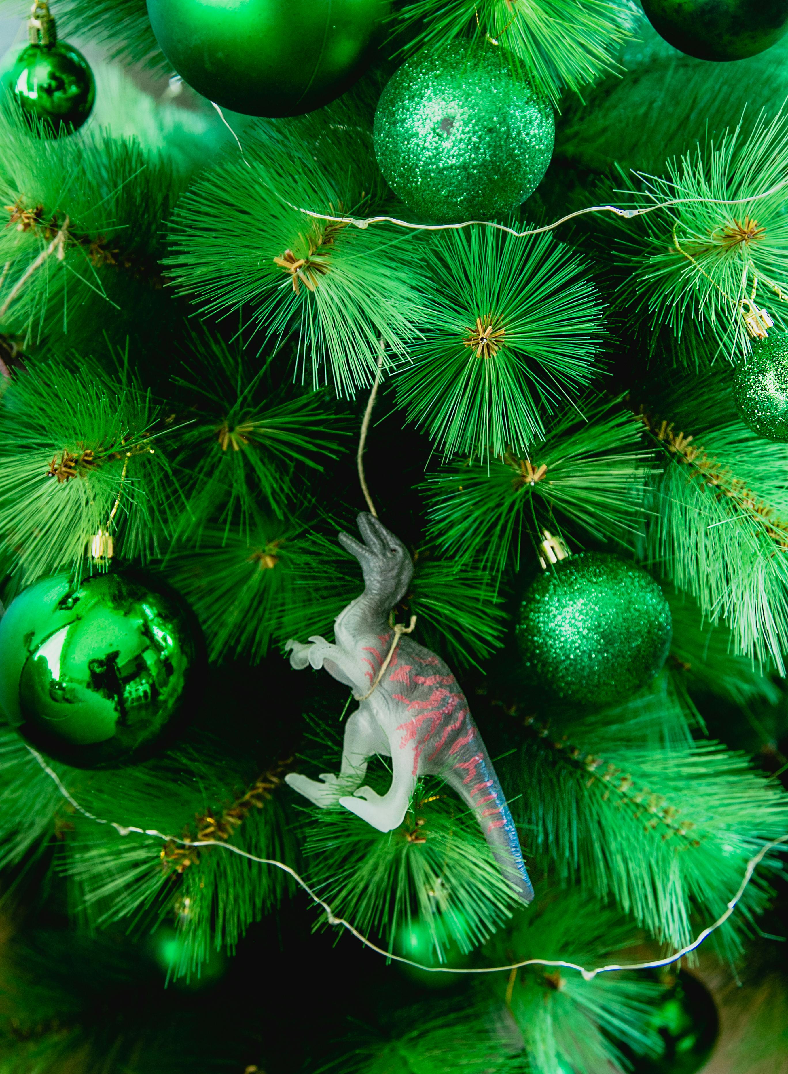 A unique Christmas tree decorated with green baubles and a dinosaur ornament, blending festive cheer and creativity.