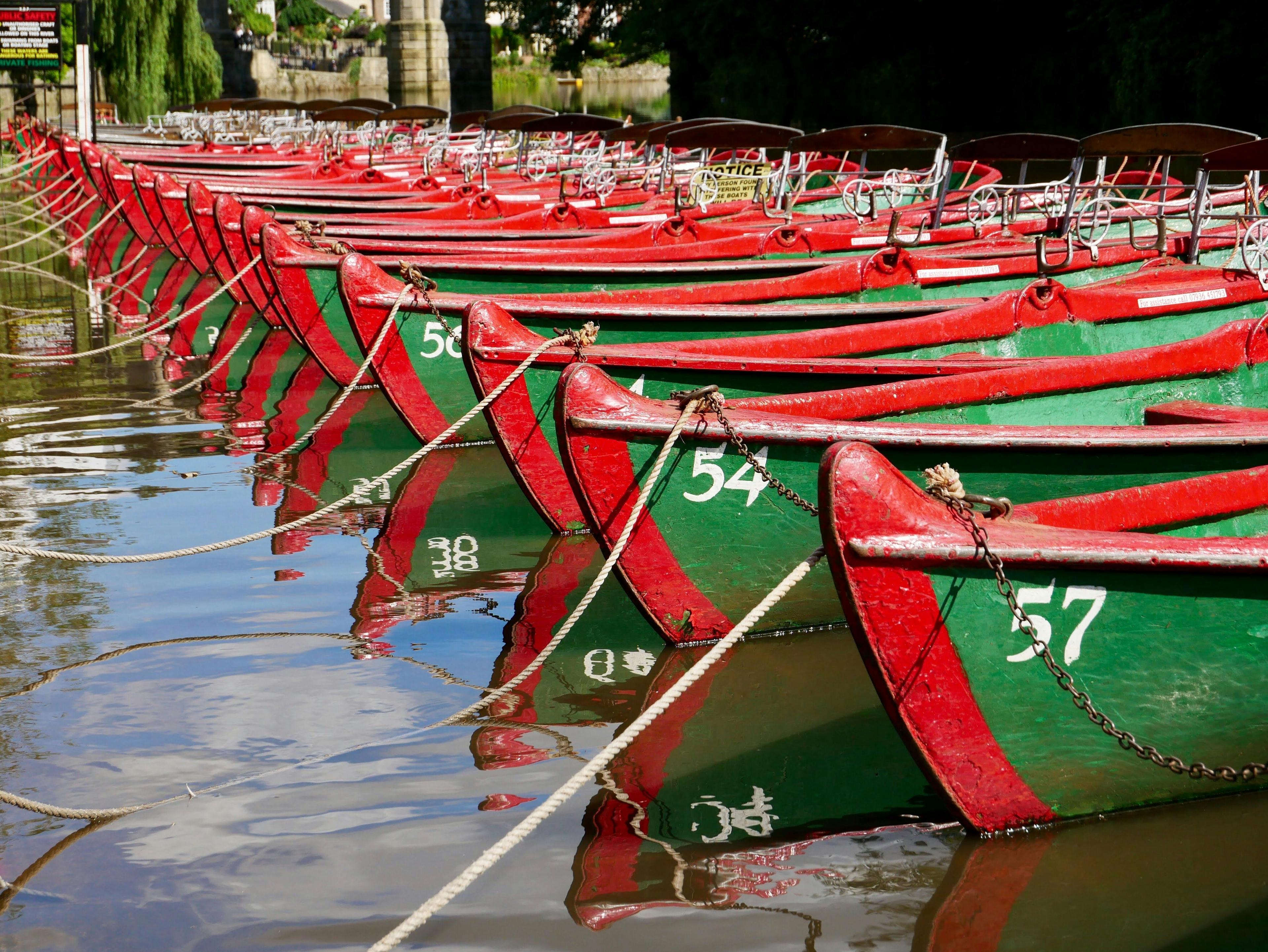 Vibrant red and green boats moored on the River Nidd, ideal for hire and leisurely river cruises.