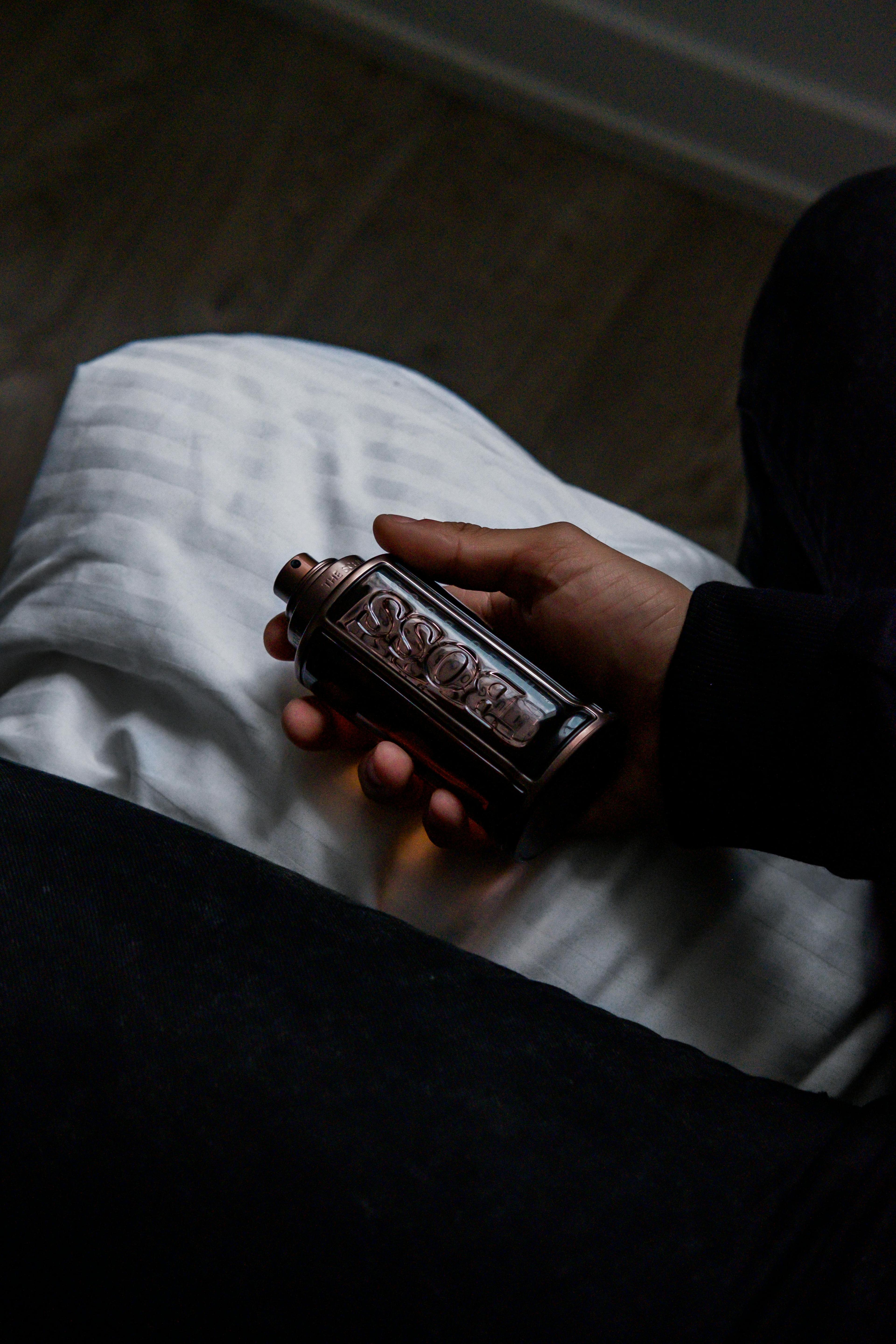 Artistic shot of a hand holding a dark-toned perfume bottle indoors, showcasing elegance and luxury.