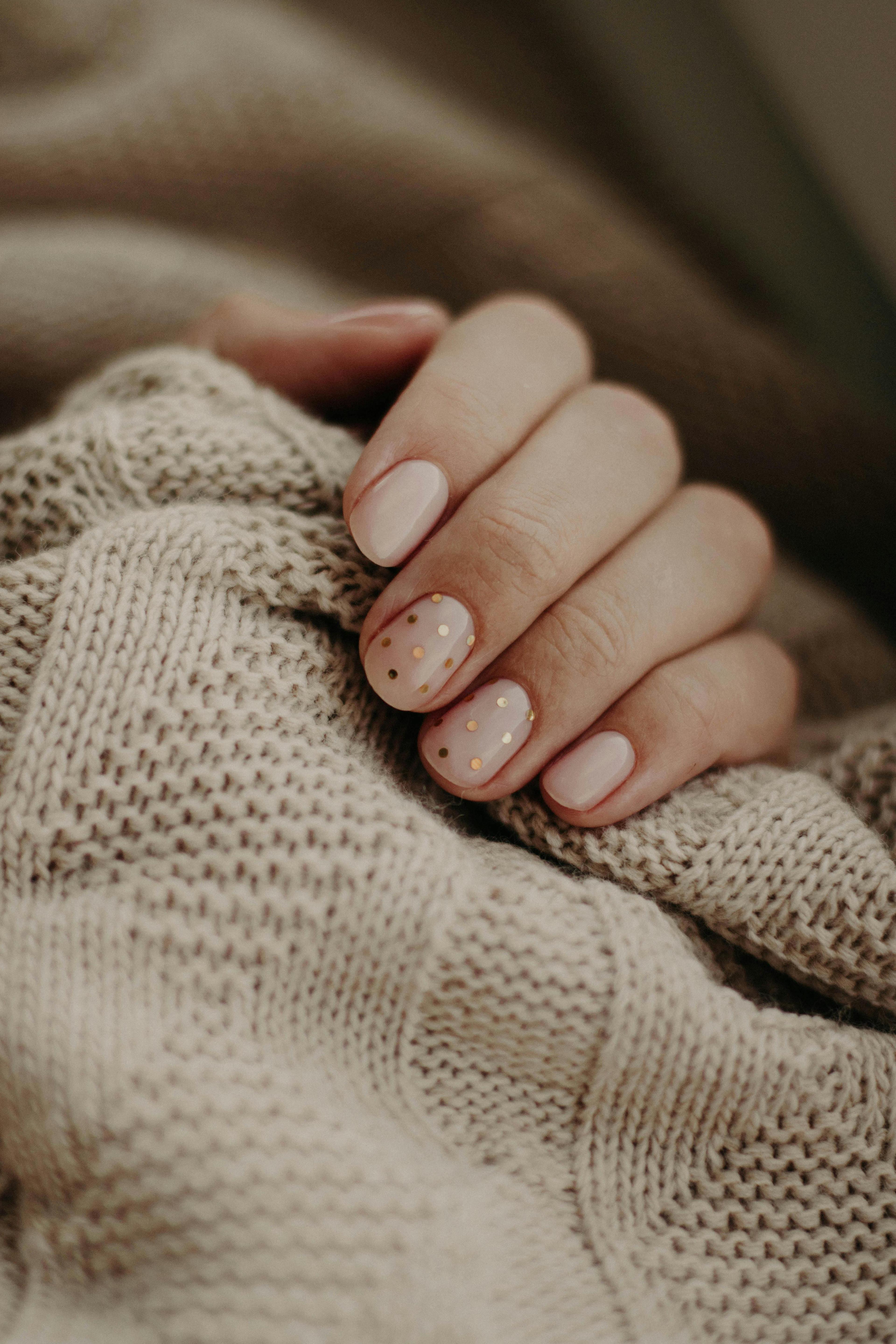 Close-up of a hand with polka dot manicured nails wrapped in a knitted sweater.