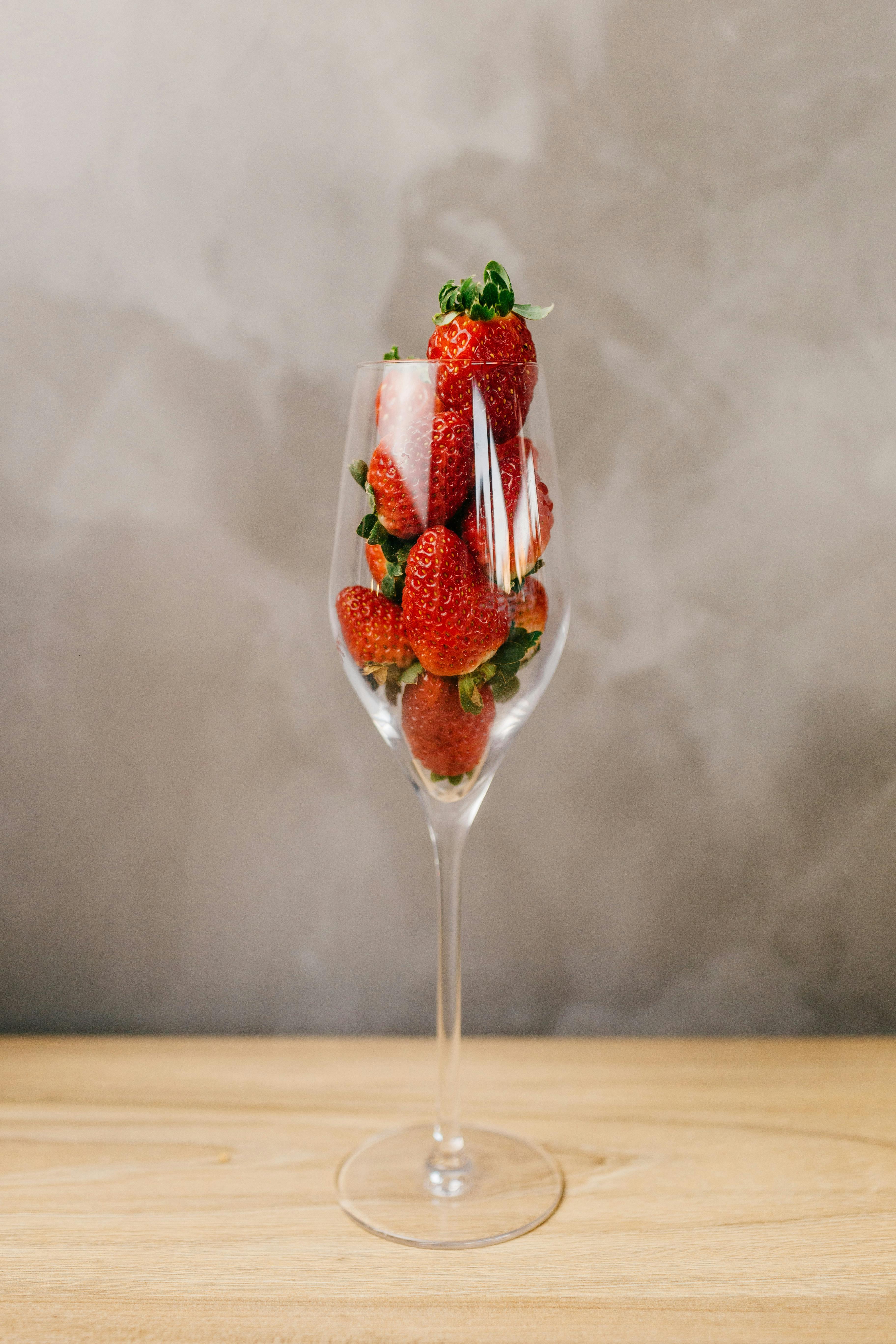 Elegant arrangement of fresh strawberries in a clear wine glass against a neutral background.