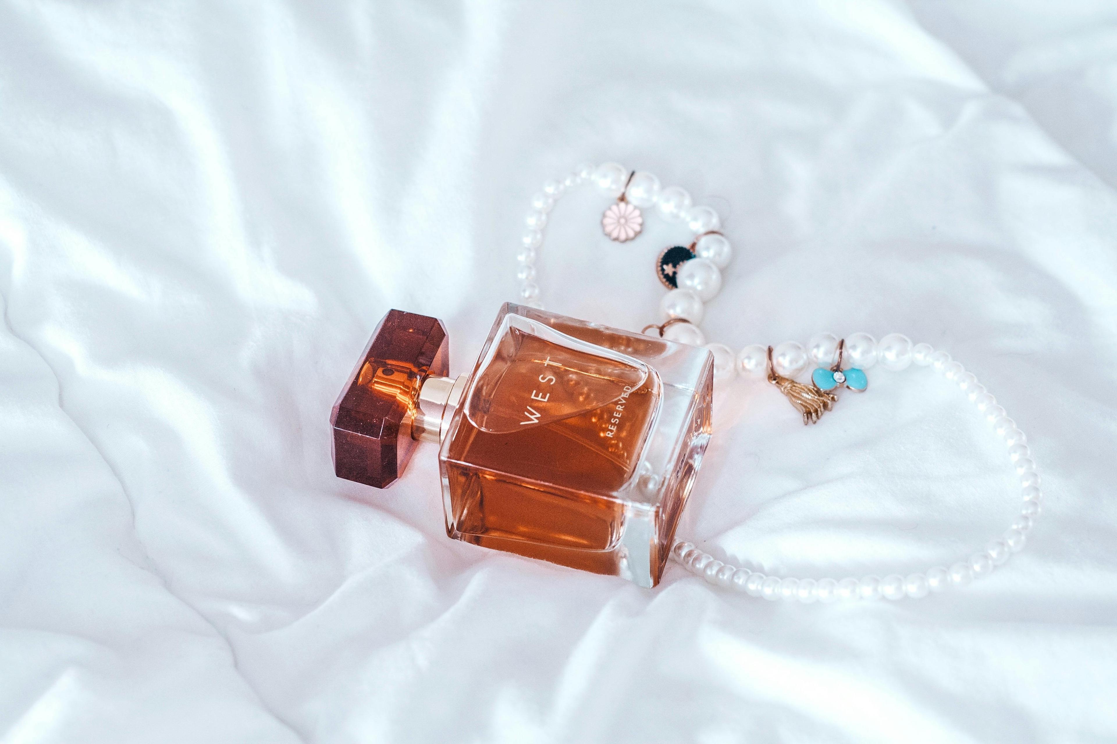 Luxury perfume bottle and pearl necklace on soft white fabric creating an elegant and fragrant aesthetic.
