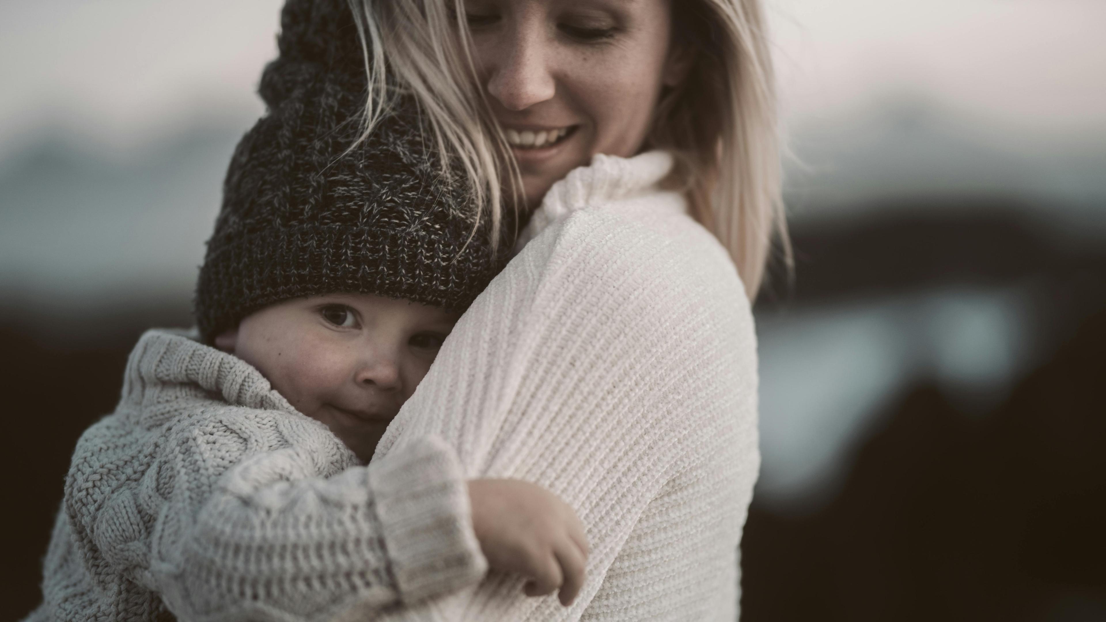 A tender moment of a mother embracing her child in cozy knitwear outdoors.