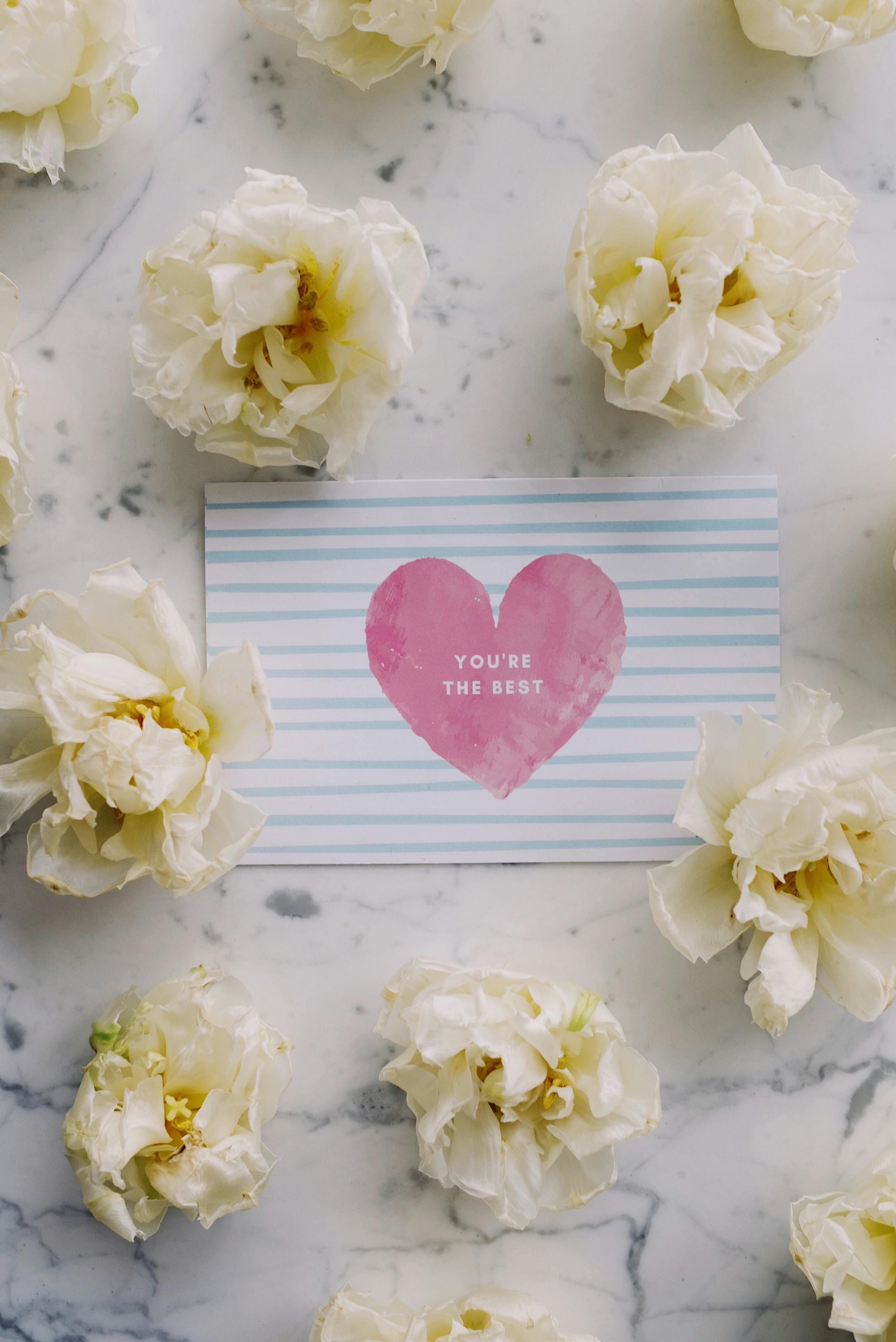 A decorative card with a heart, surrounded by white flowers on a marble surface.