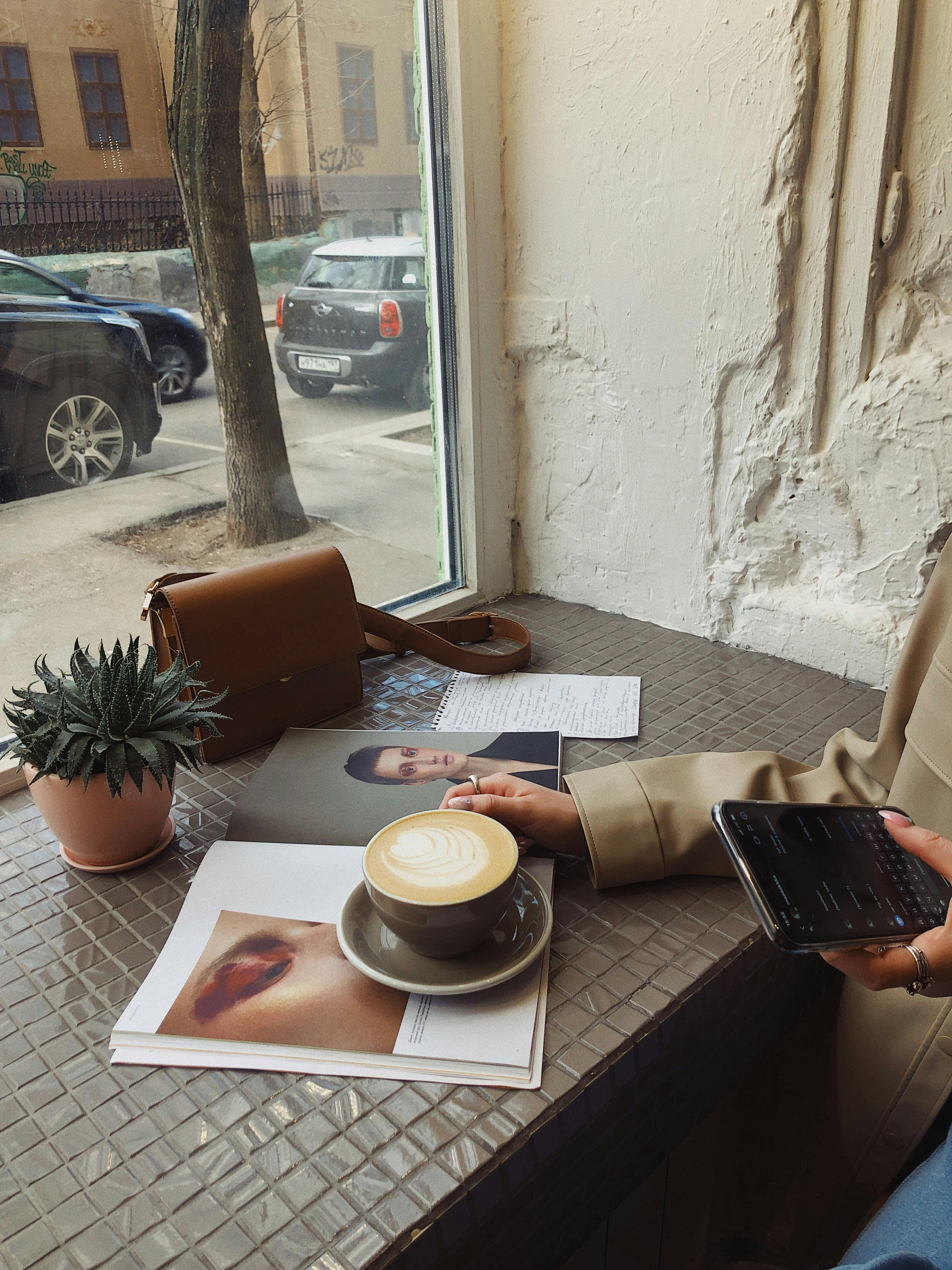 Crop of unrecognizable female tourist in casual wear surfing internet and flipping magazine while drinking coffee in sidewalk cafe