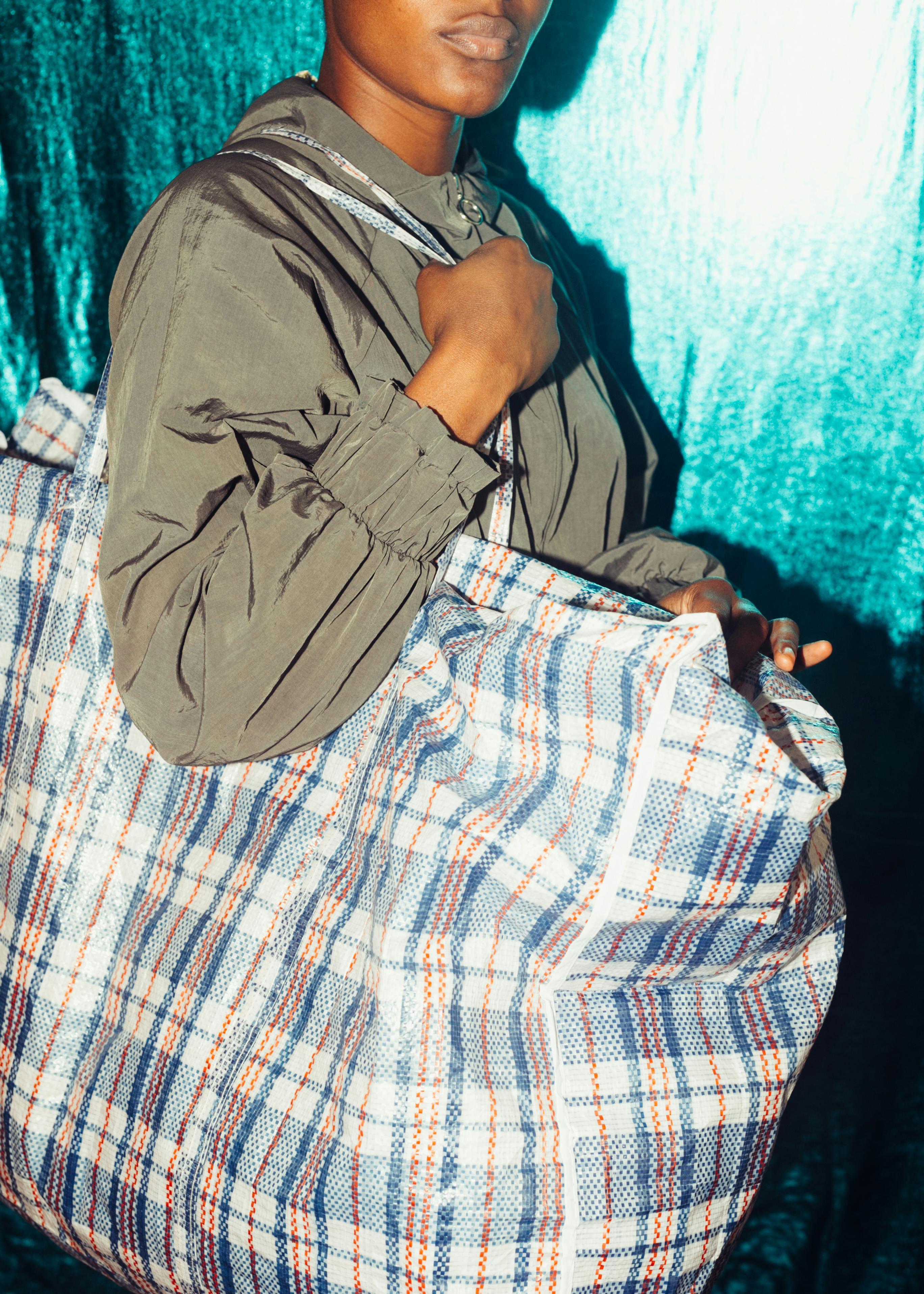 Anonymous black person with large plaid bag standing by blue wall