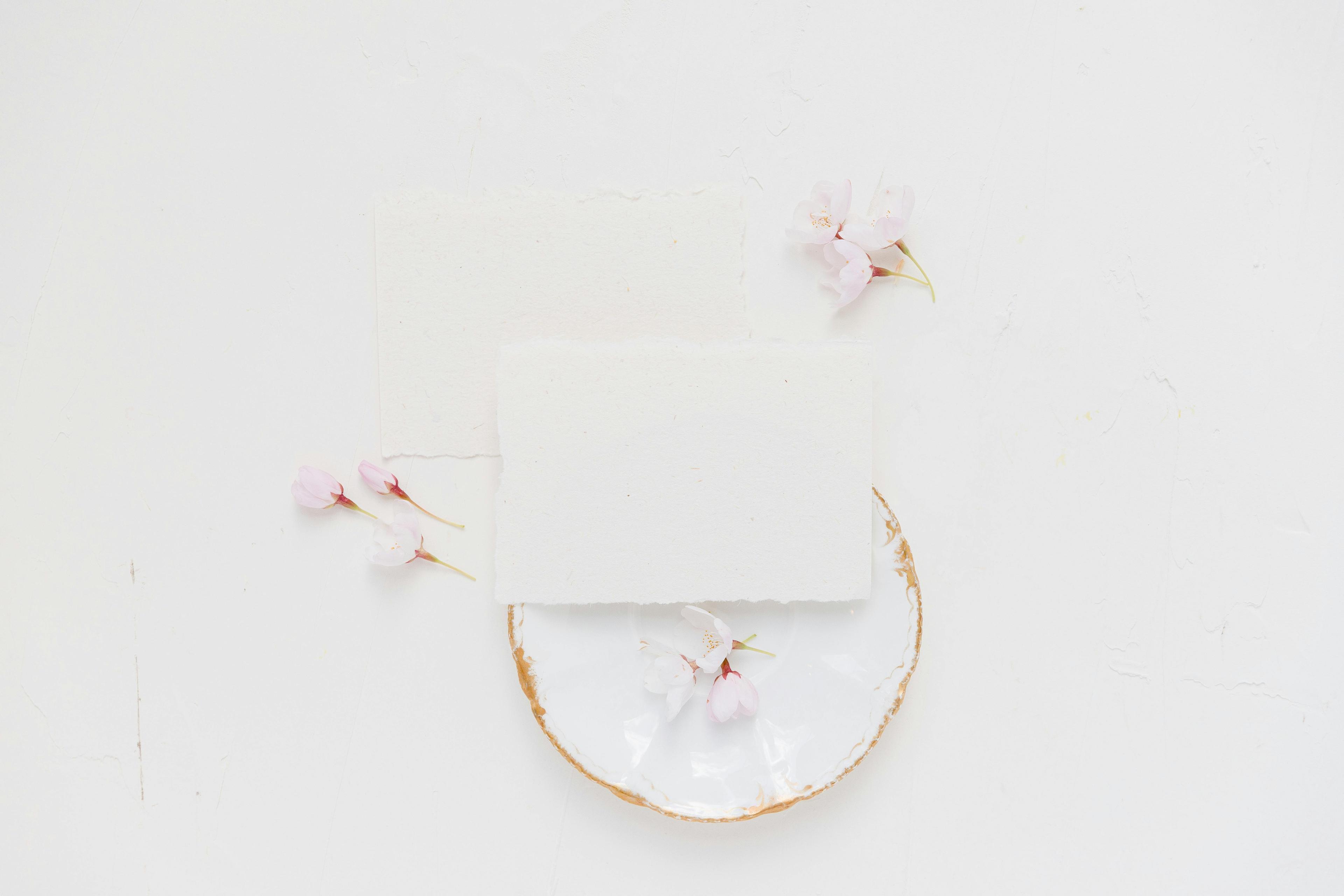 Delicate cherry blossoms on blank cards and ceramic plate in a soft minimalist flat lay.