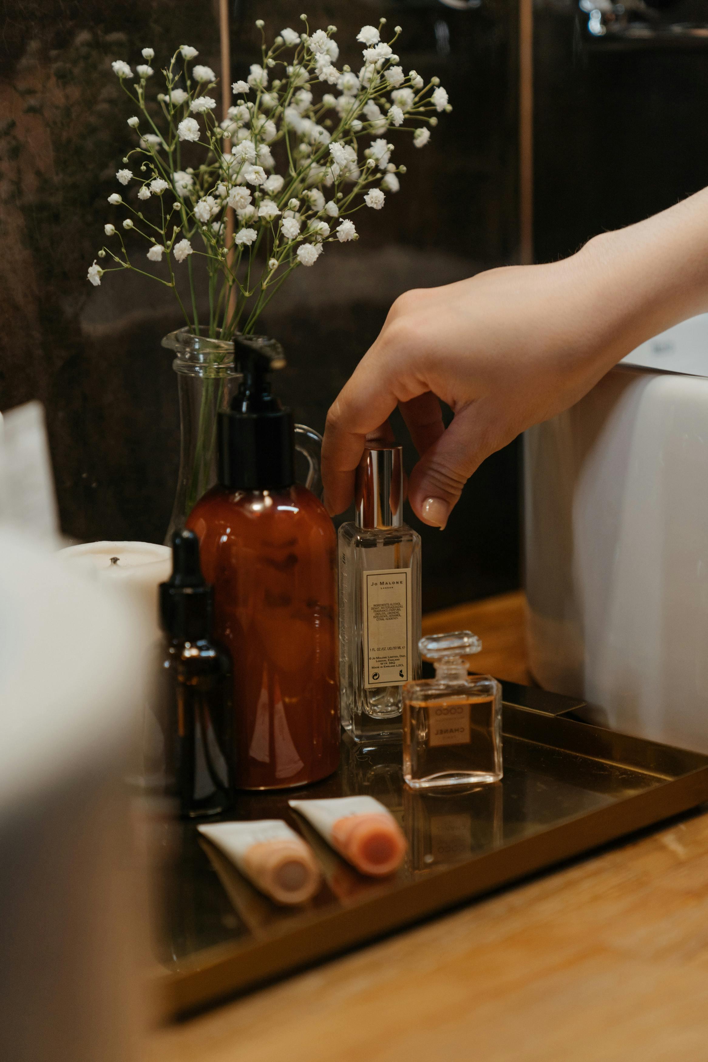 A serene bathroom scene featuring stylish skincare products and a hand reaching for a perfume bottle.