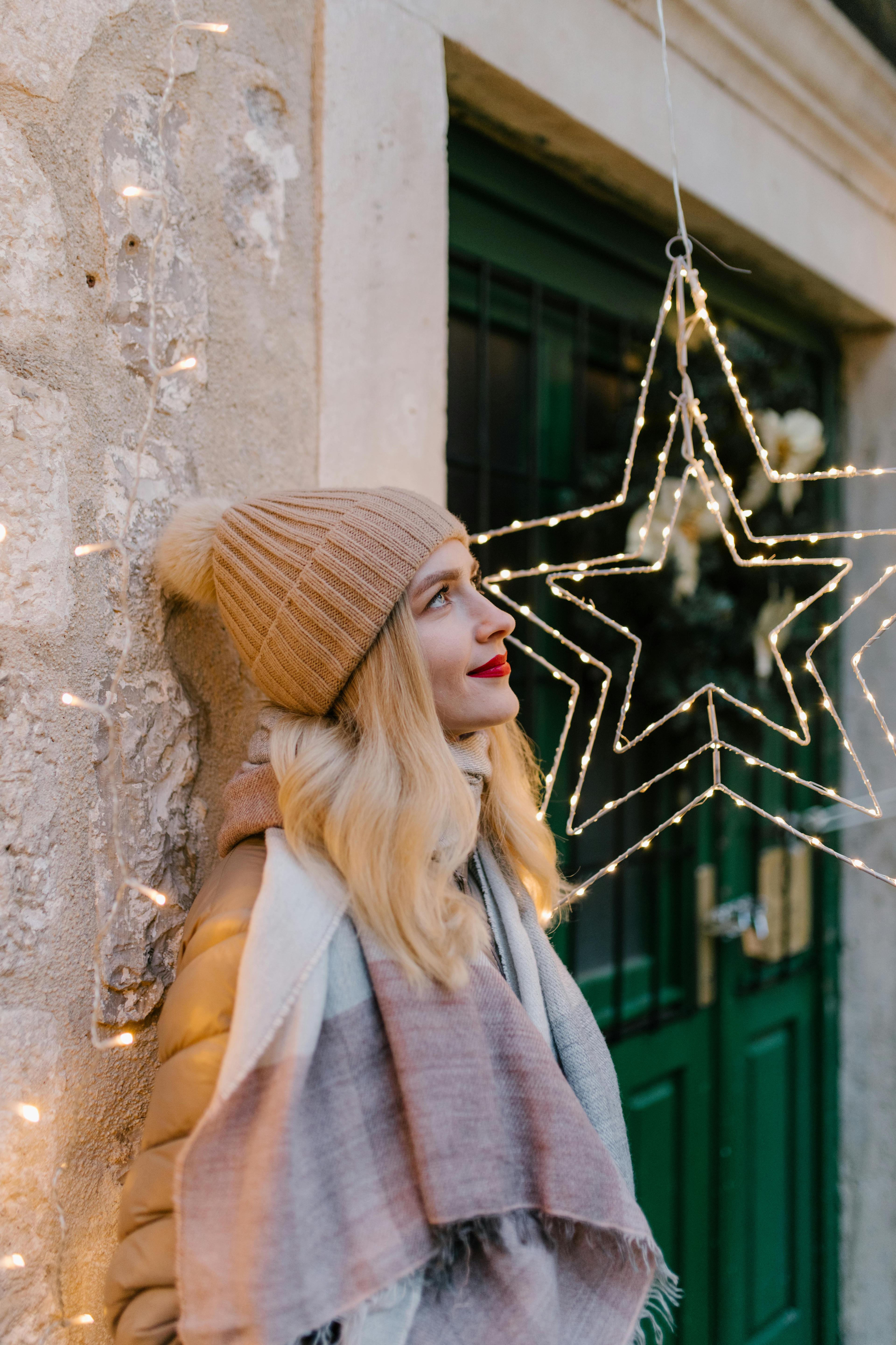 Young woman smiling by festive star lights outdoors, embracing winter charm.