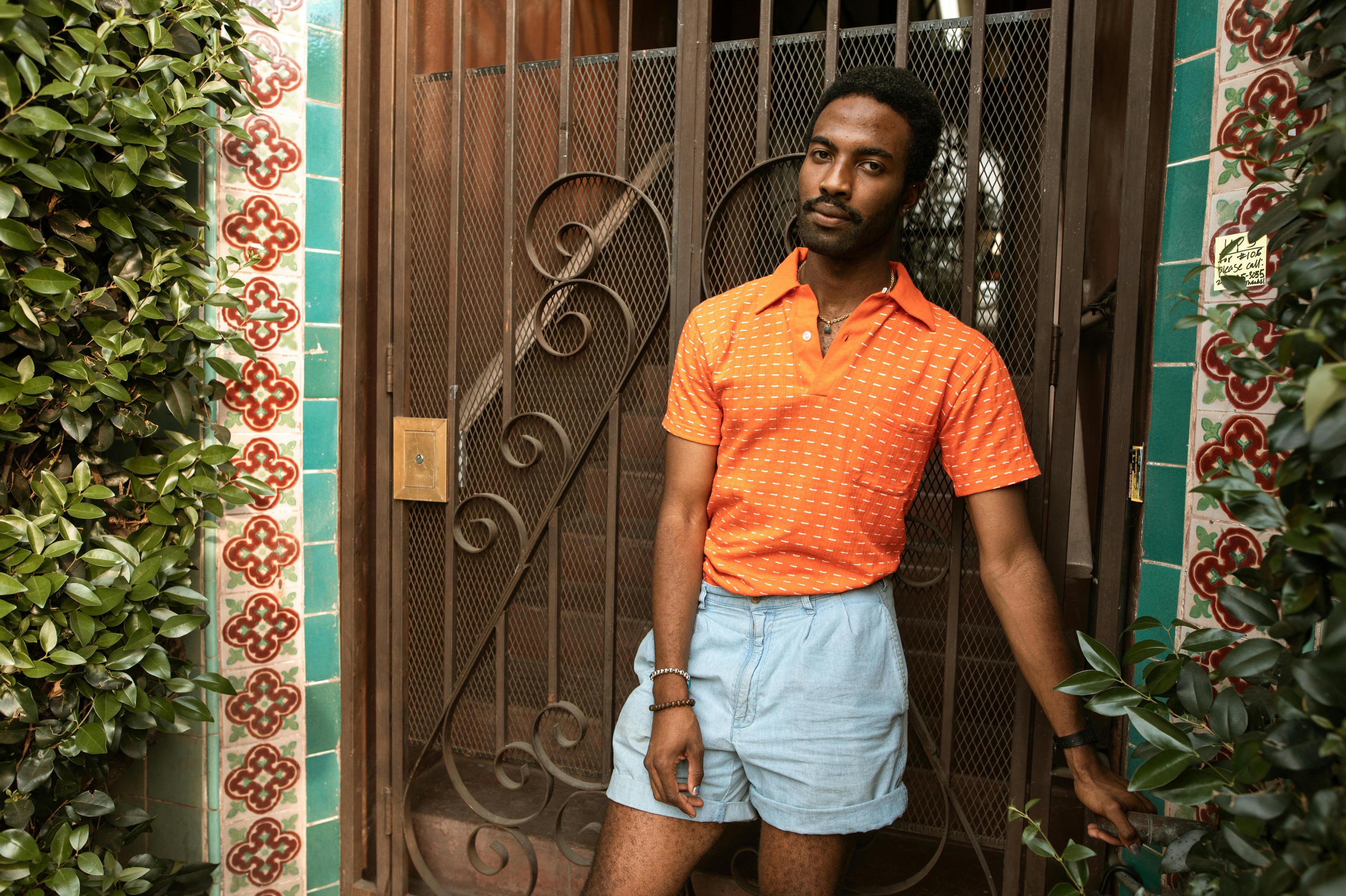 Man in vibrant outfit posing by a beautifully tiled entrance, exuding fashion and confidence.