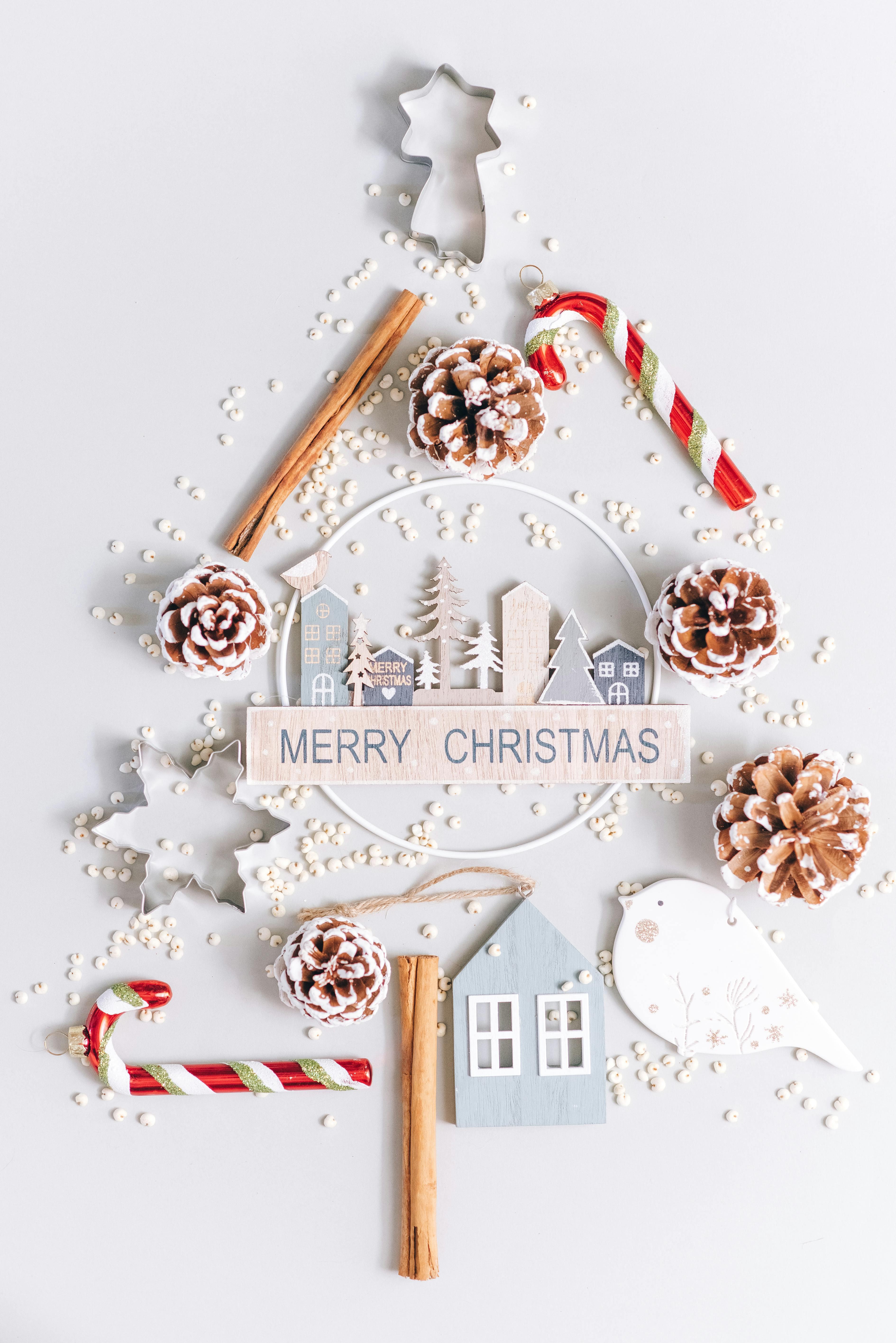 Festive flatlay of Christmas tree with ornaments, candy canes, and pinecones on white background.