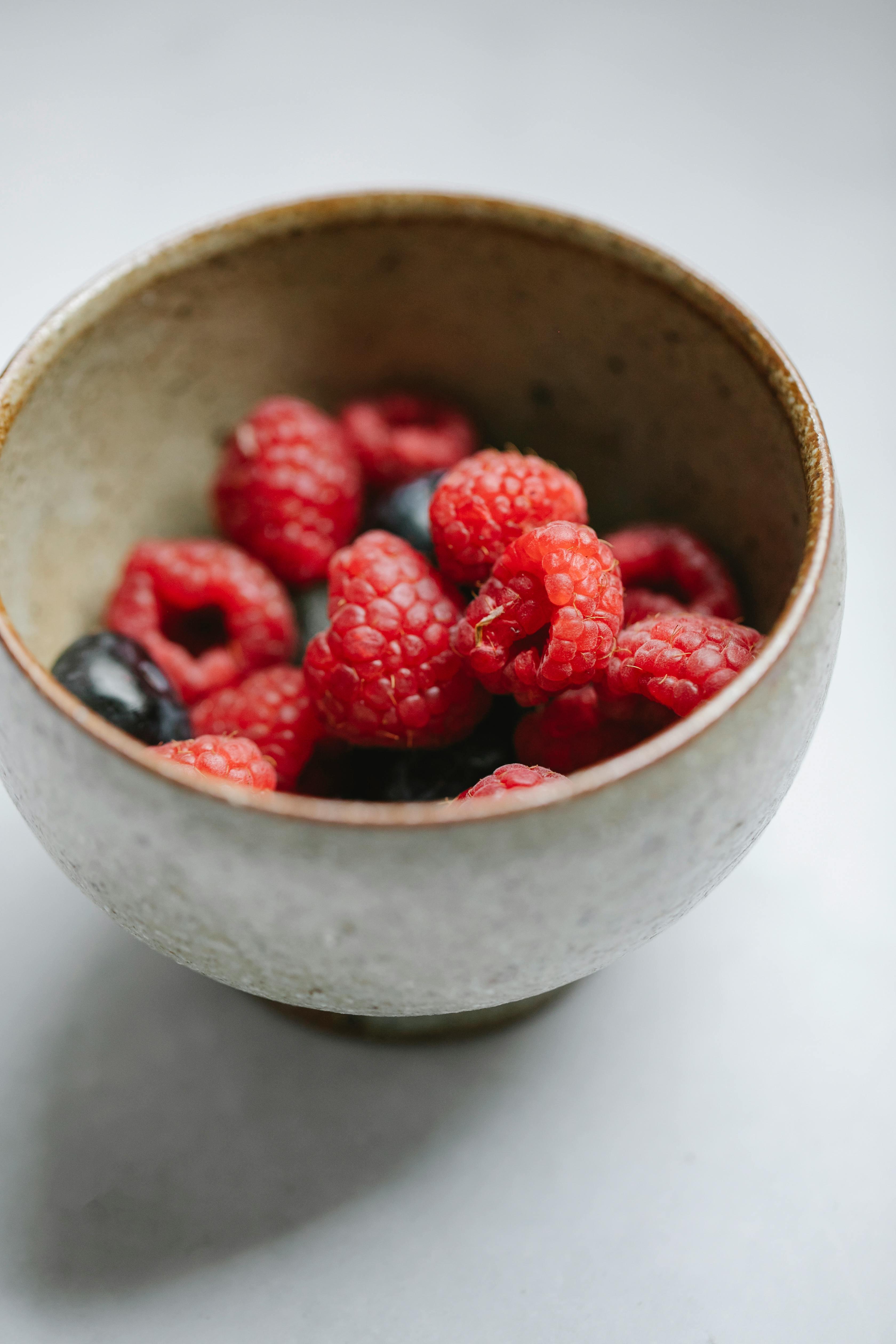 From above of tasty fresh raspberries and blueberries in bowl for healthy meal placed on white table