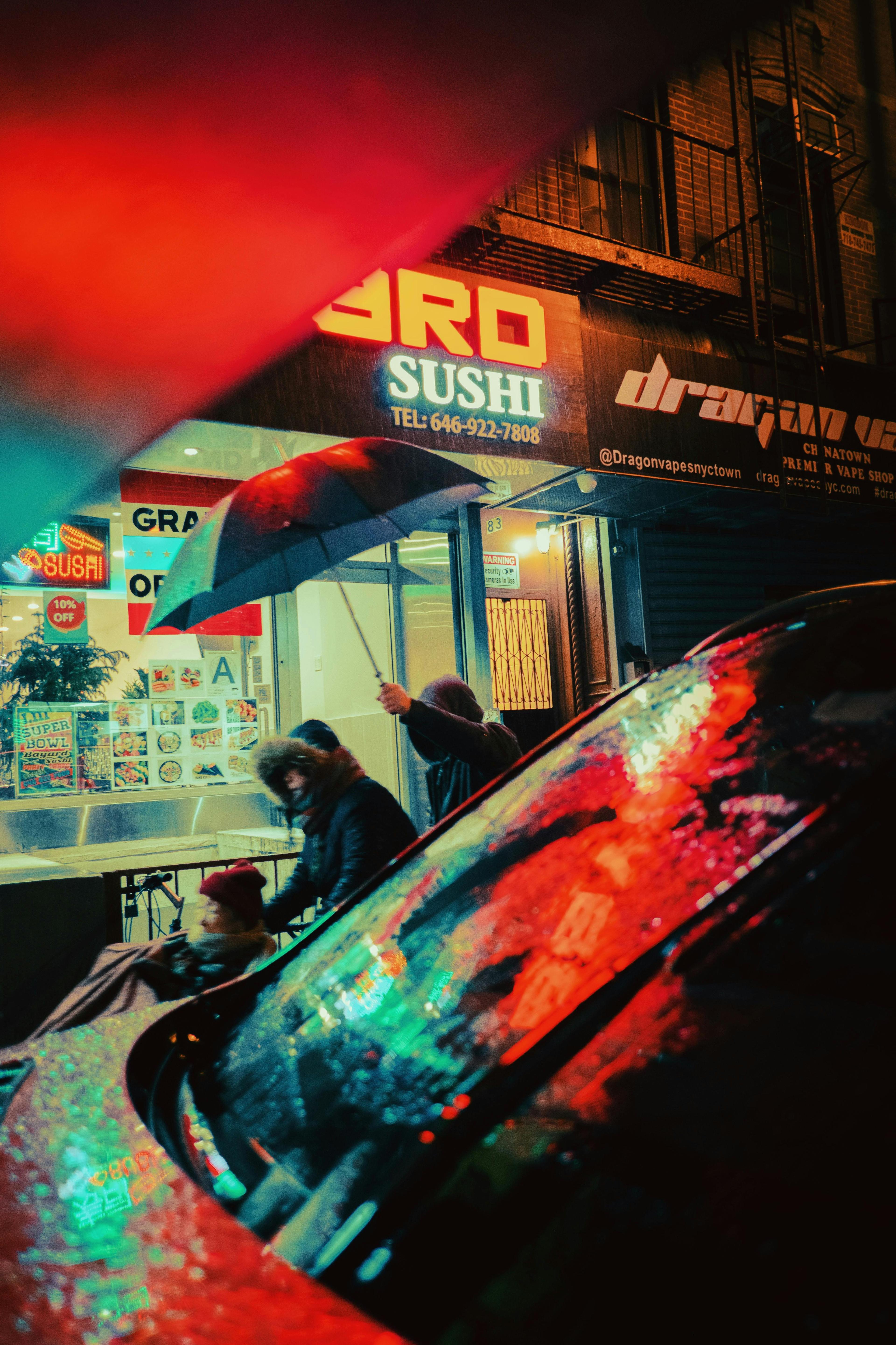 Colorful city street scene at night with people walking under umbrella, reflecting neon lights.