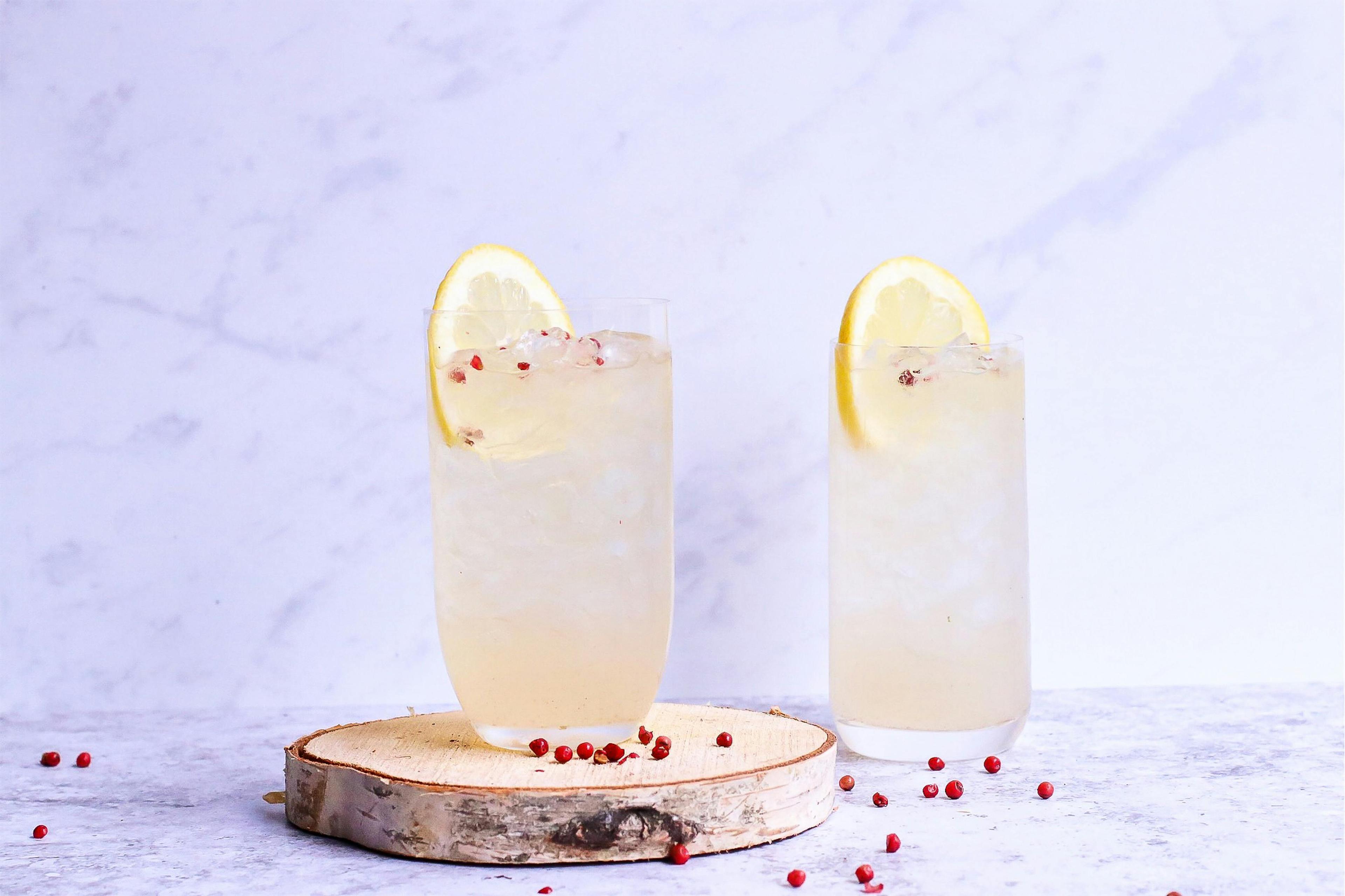 Glasses of delicious cold lemonade decorated with lemon slice and berries on wooden board in light studio