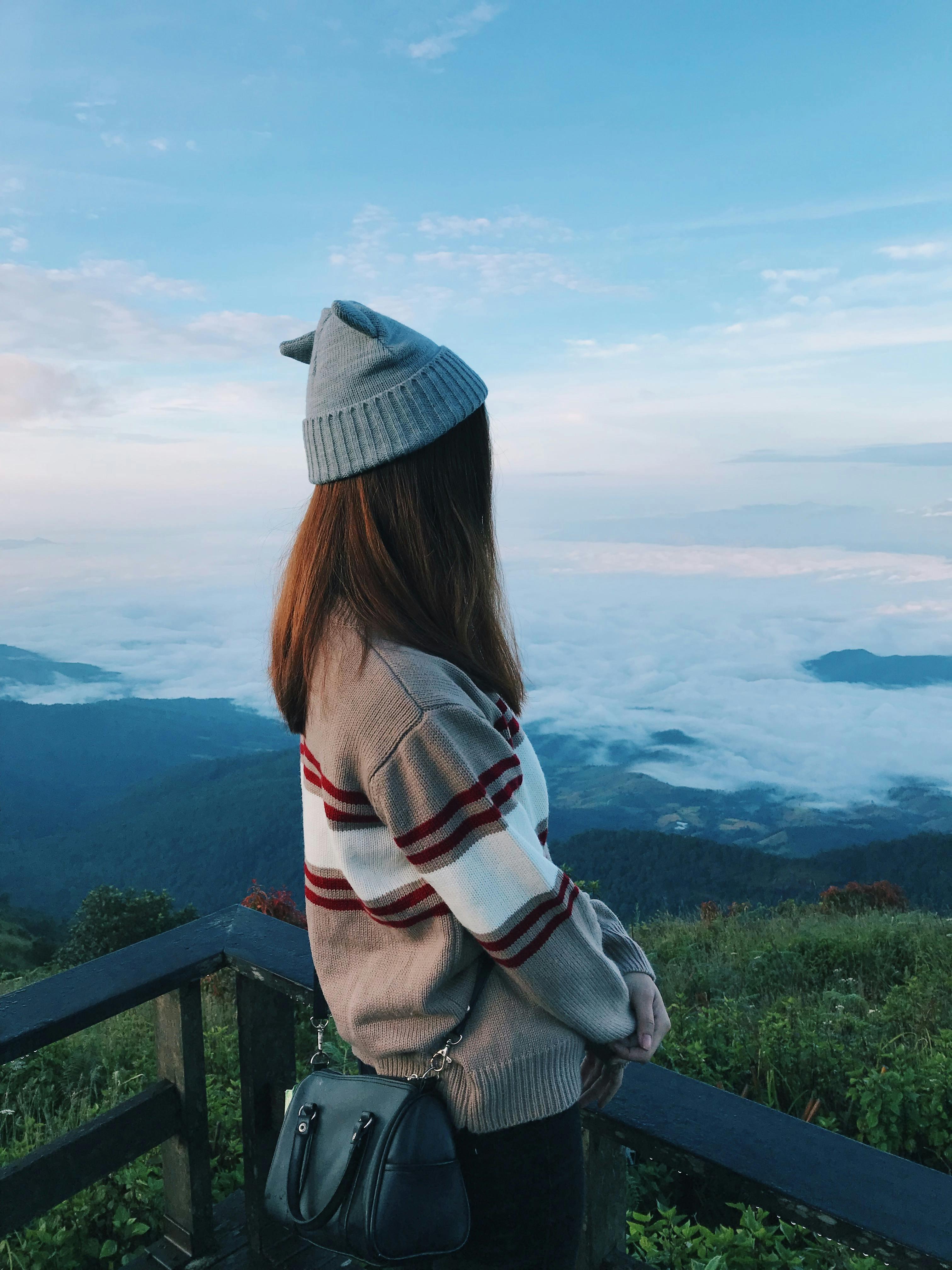 A woman stands on a viewing platform overlooking a scenic mountain and cloud landscape in Chiang Mai, Thailand.