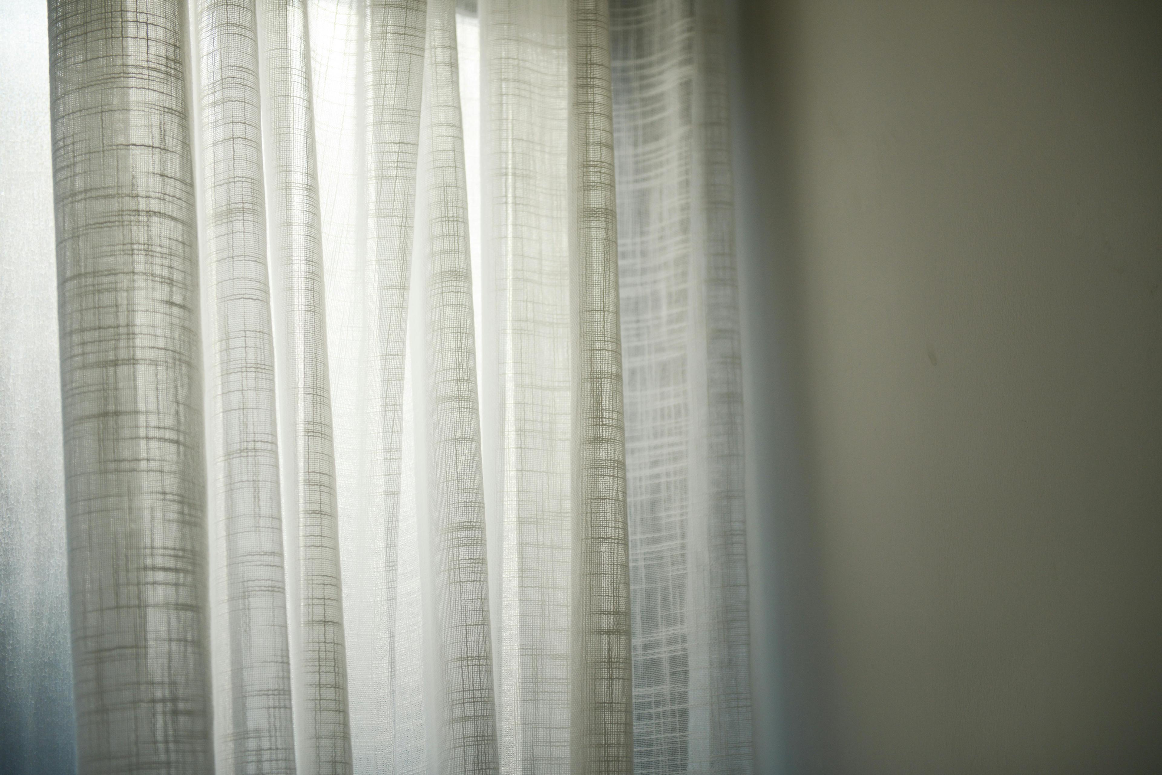 Sheer white curtains gently lit by daylight create subtle shadows on the wall.